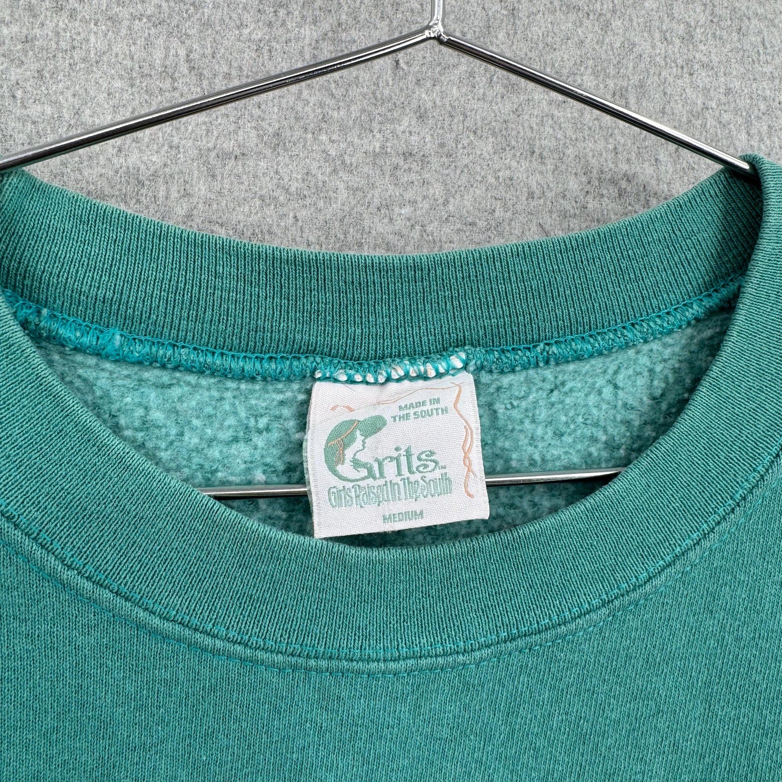 Teal sweatshirt with a brand tag on a hanger. size Medium