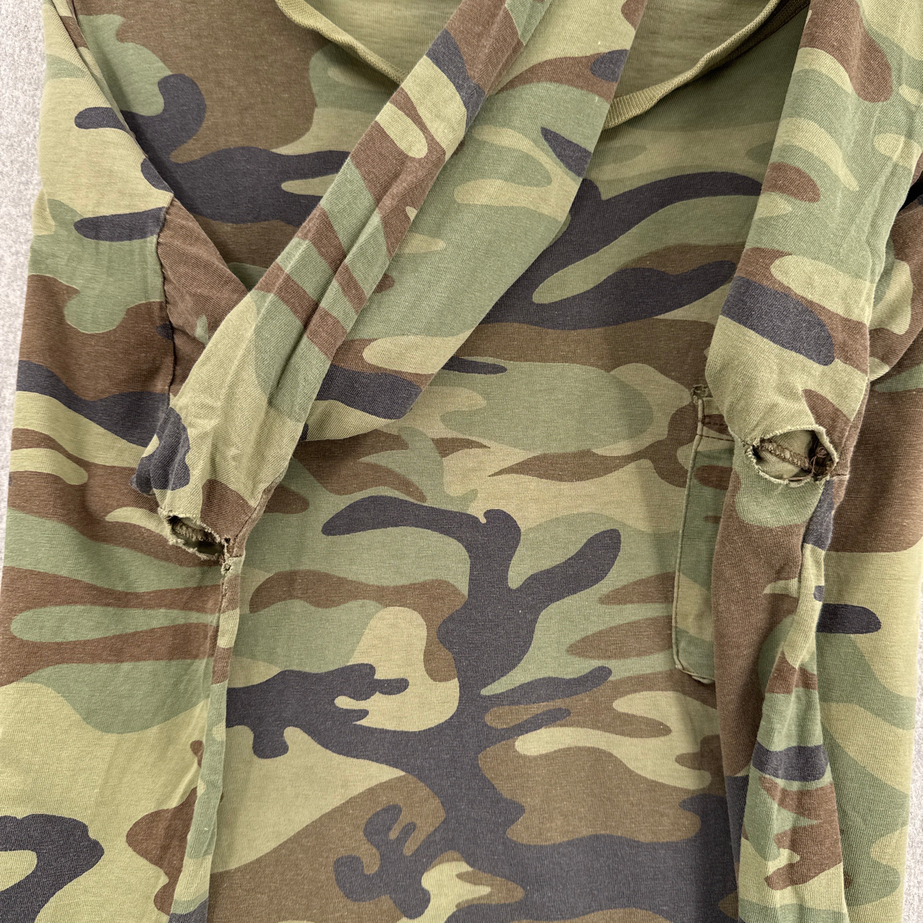 Close-up of camouflage fabric with a pattern of green, brown, and black. Armpits with holes in it