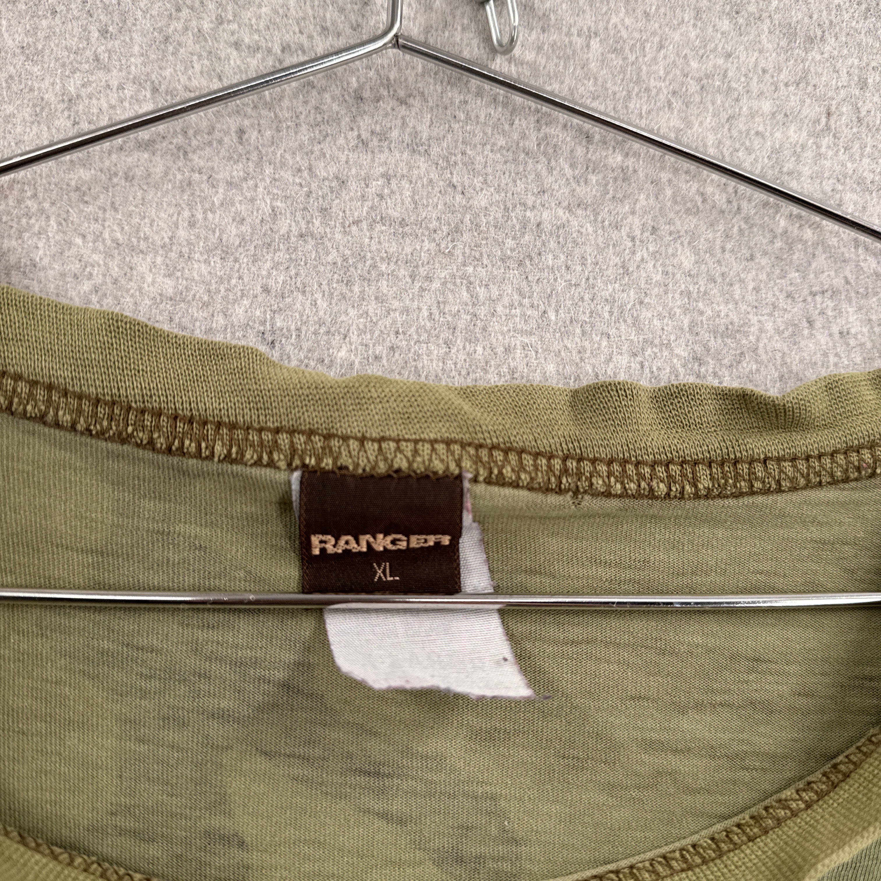 Close-up of a green fabric with a label on a textured gray background. Size XL brand name Ranger