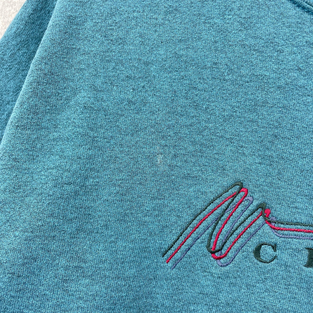 Close-up of a teal fabric with an embroidered logo on a textured background. small stain spot