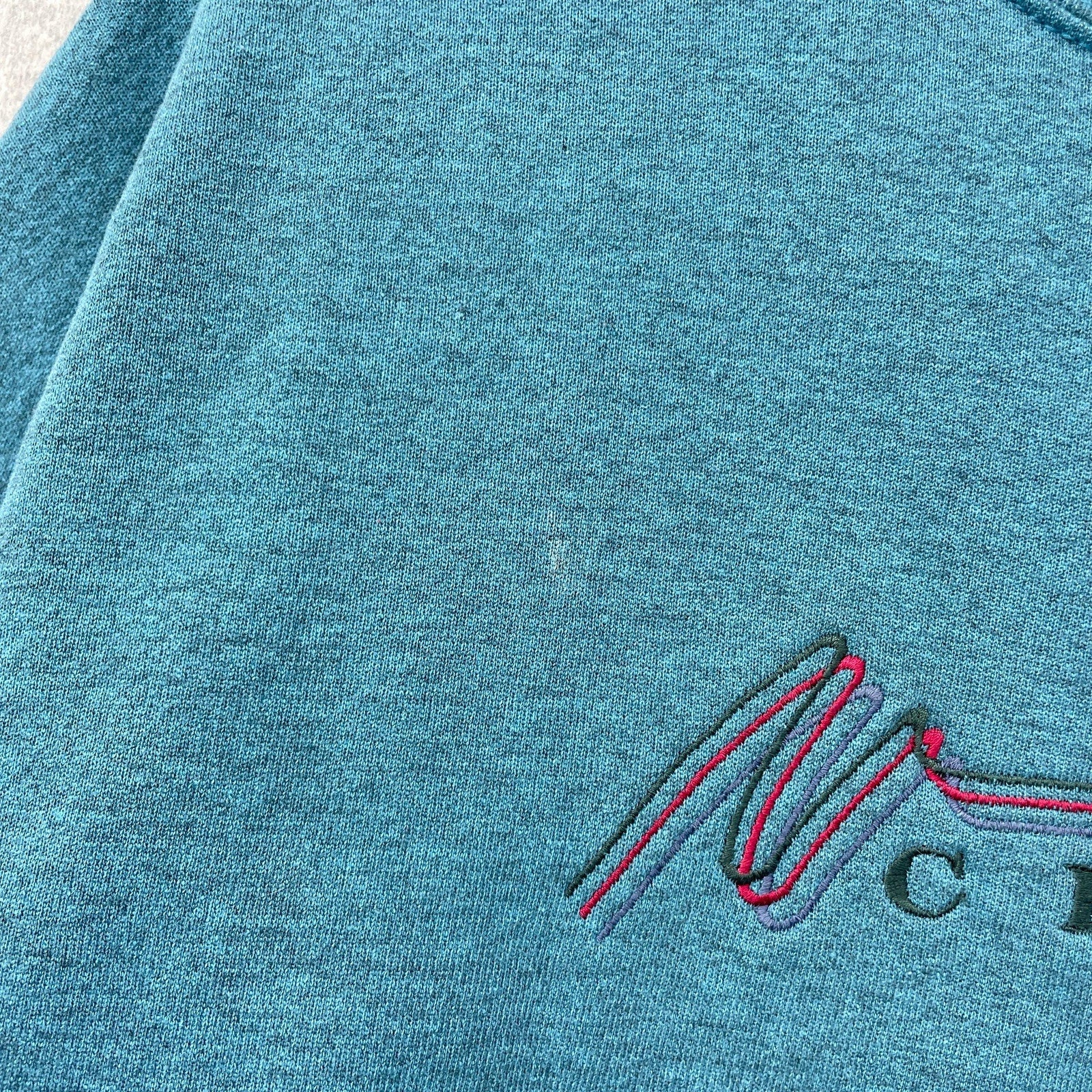 Close-up of a teal fabric with an embroidered logo on a textured background. small stain spot