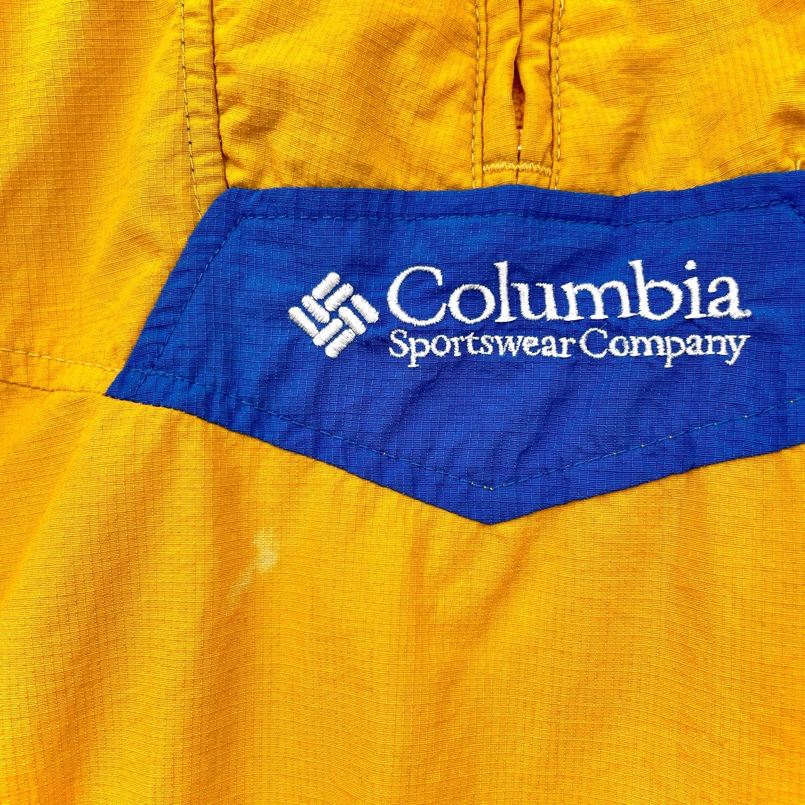 Close-up of Columbia Sportswear Company logo on a yellow garment. small stain spot near front logo