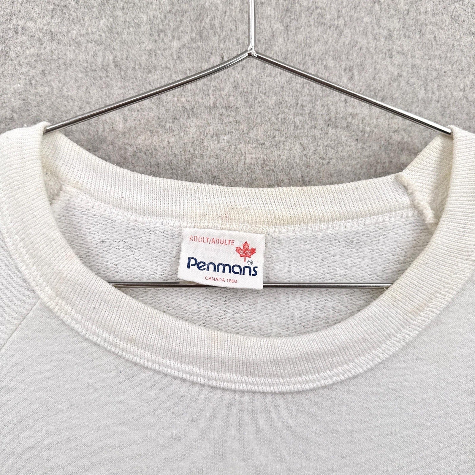 White sweatshirt with a Penmans label on a hanger against a gray background
