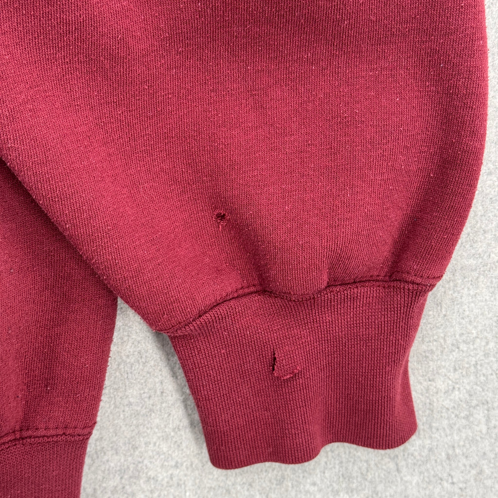 Close-up of a maroon sweatshirt sleeve with 2 holes/tears on a light gray background.