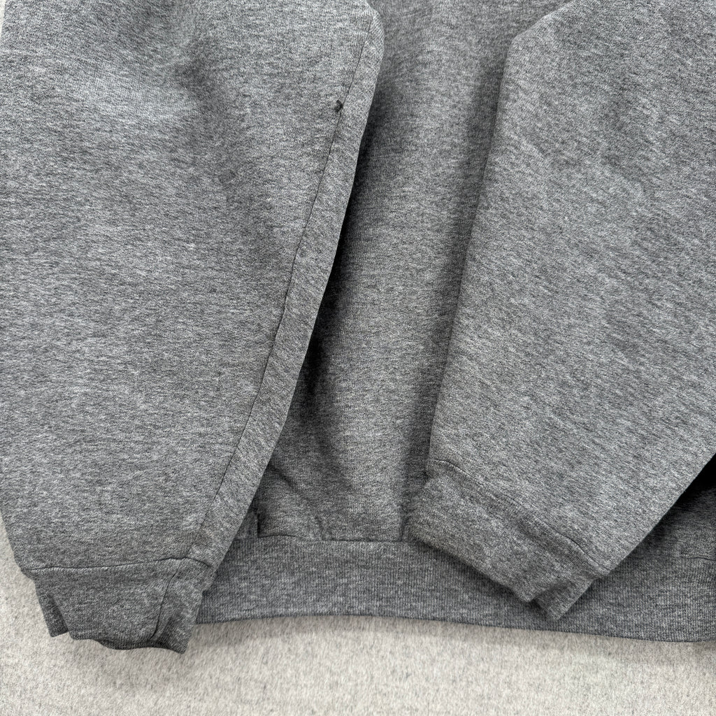Gray sweatshirt folded on a light gray surface, sleeves showing signs of wear with some stain spots