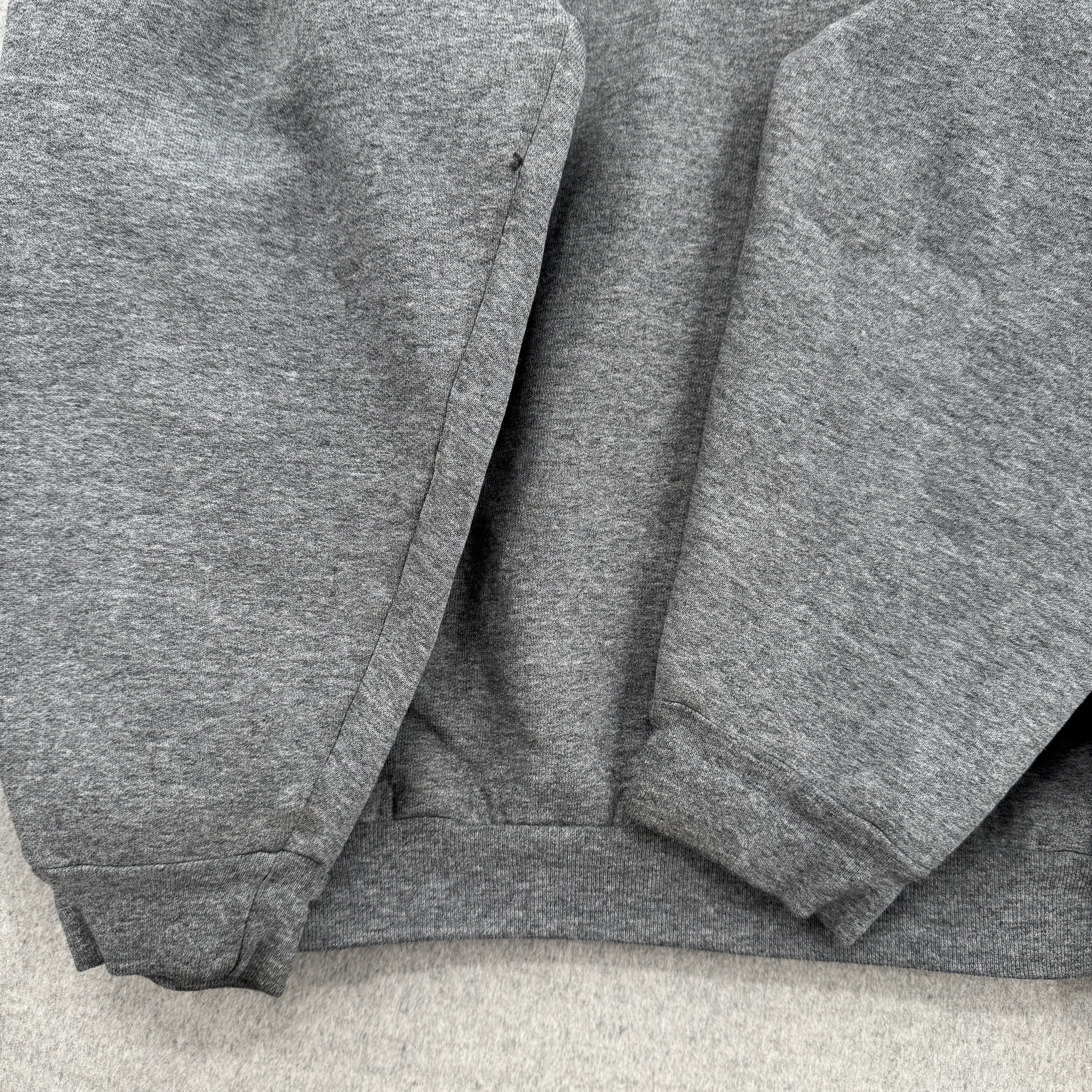 Gray sweatshirt folded on a light gray surface, sleeves showing signs of wear with some stain spots