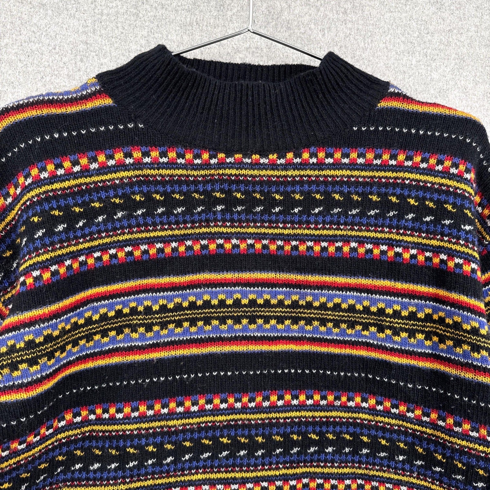 Black sweater with colorful striped pattern on a hanger against a gray textured background