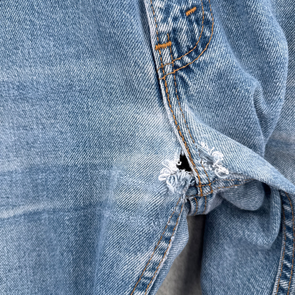Close-up of blue denim fabric with frayed edge. Hole in crotch