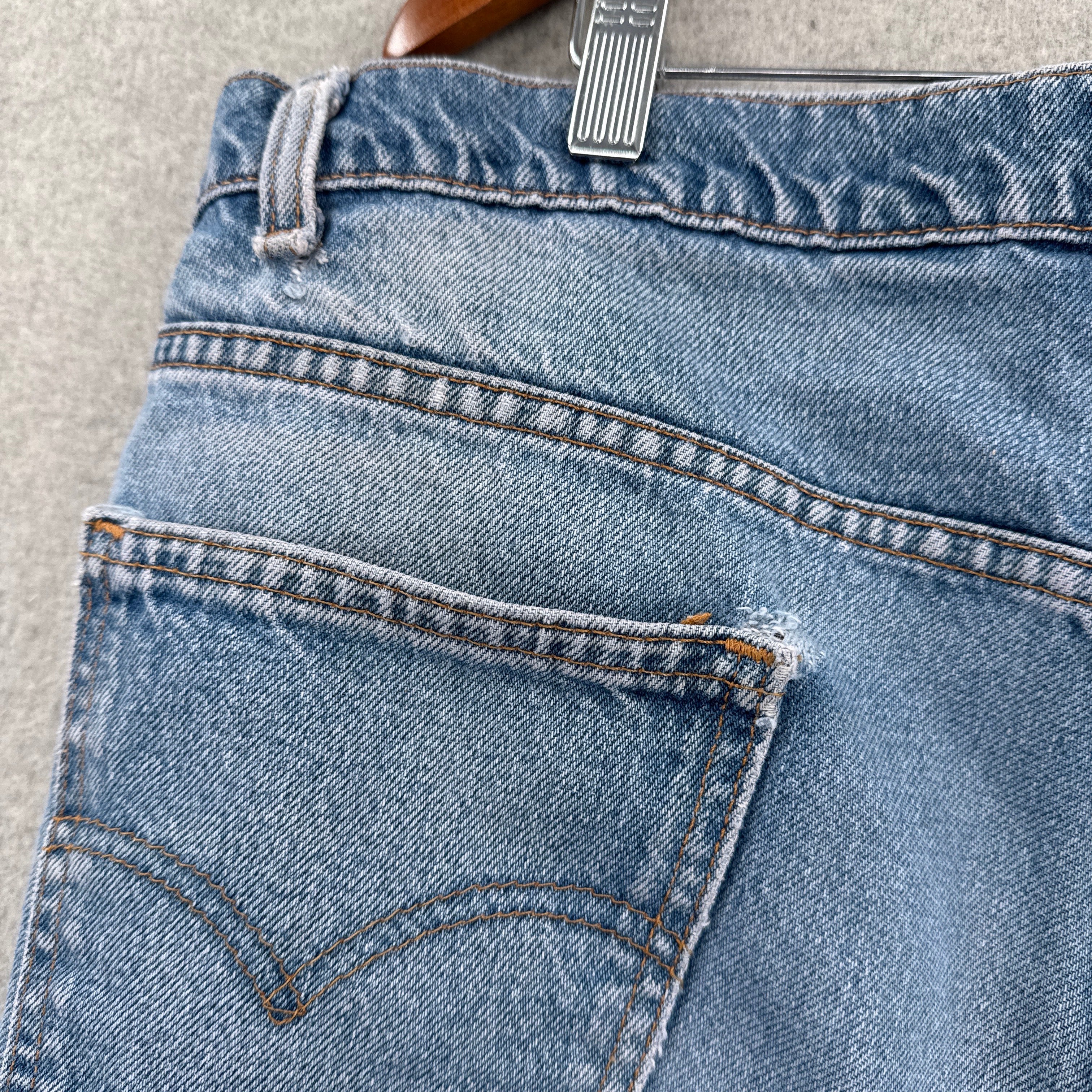 Close-up of blue jeans with stitching details on a gray surface. small rips near pocket