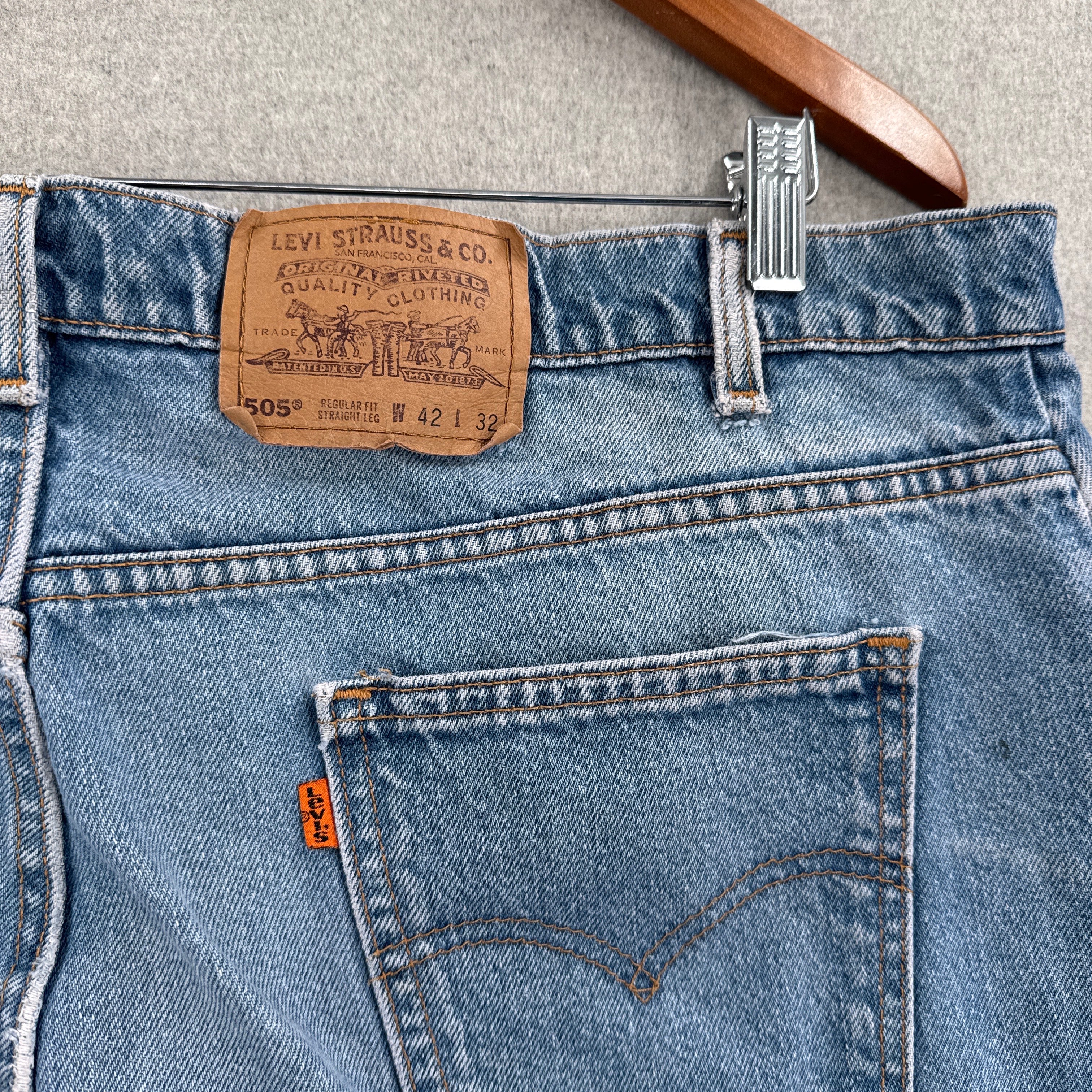 Close-up of Levi's jeans with brand label and hanger on a neutral background. Orange tab 505