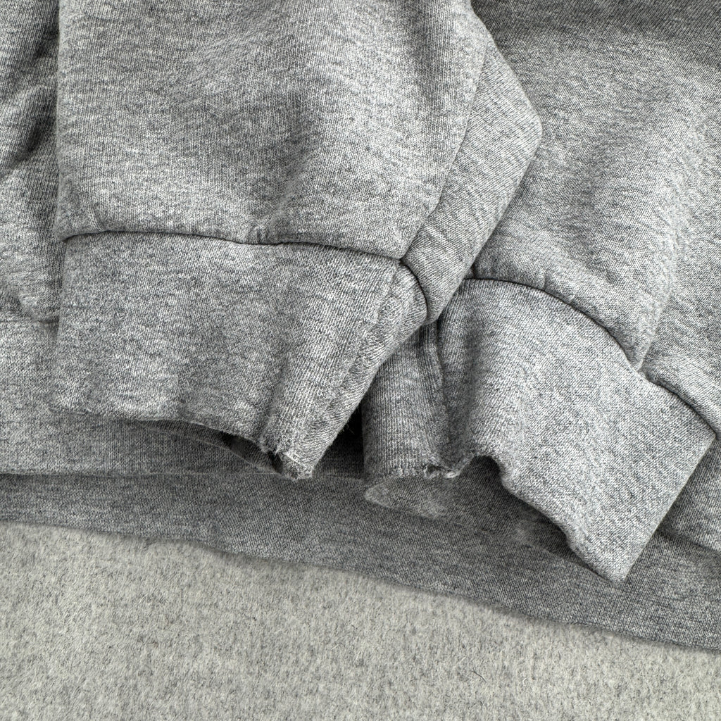 Stack of gray sweatshirts on a gray surface, fraying at bottom of sleeves