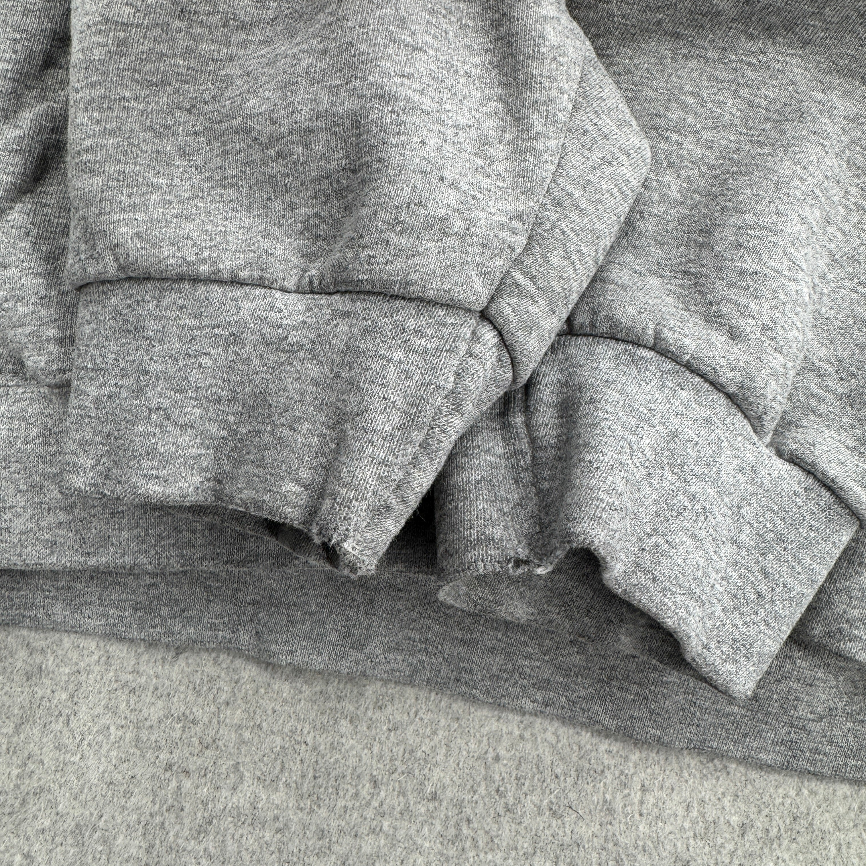 Stack of gray sweatshirts on a gray surface, fraying at bottom of sleeves
