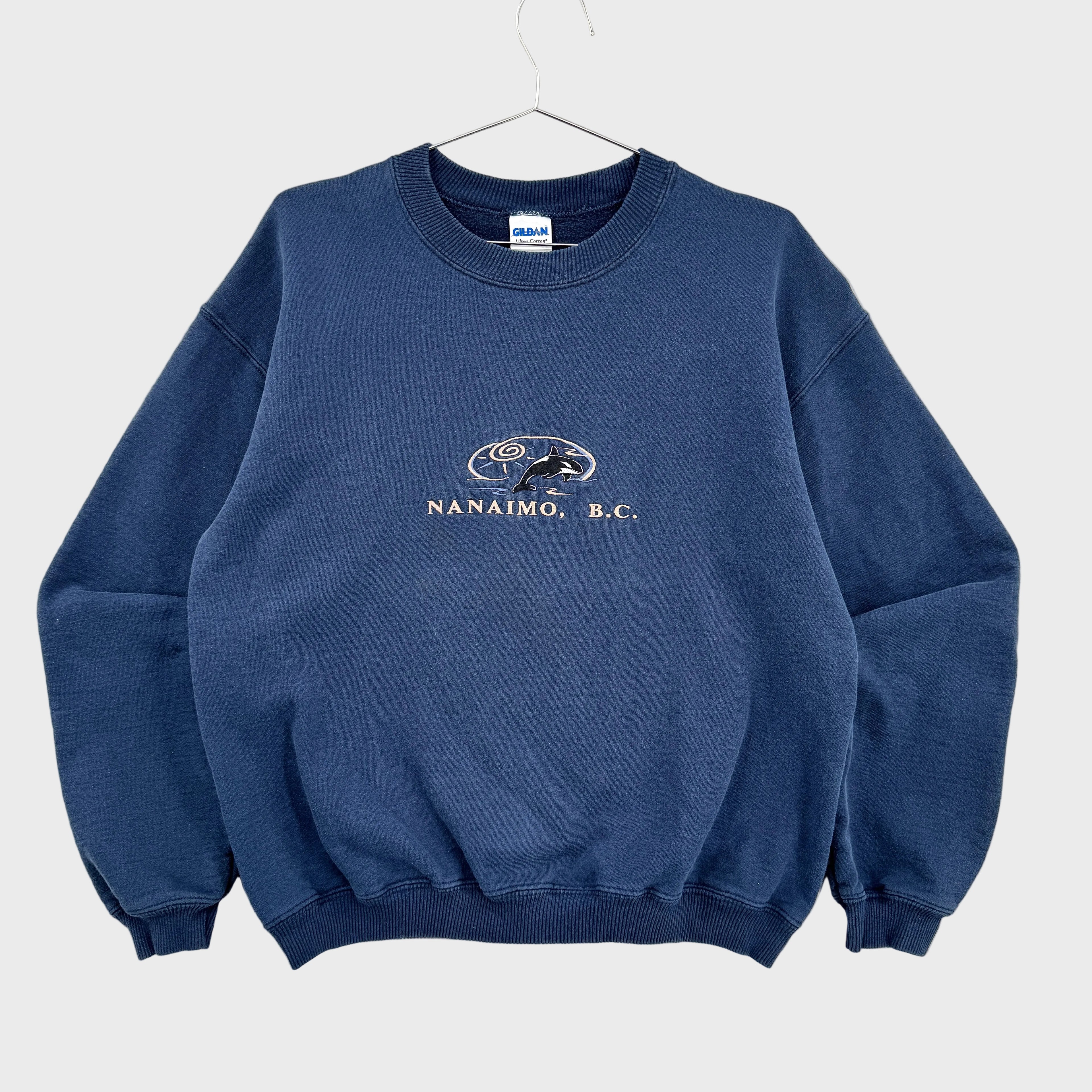 Blue sweatshirt with 'Nanaimo, B.C.' text and logo on a gray background. British Columbia souvenir with Orca Killer Whale