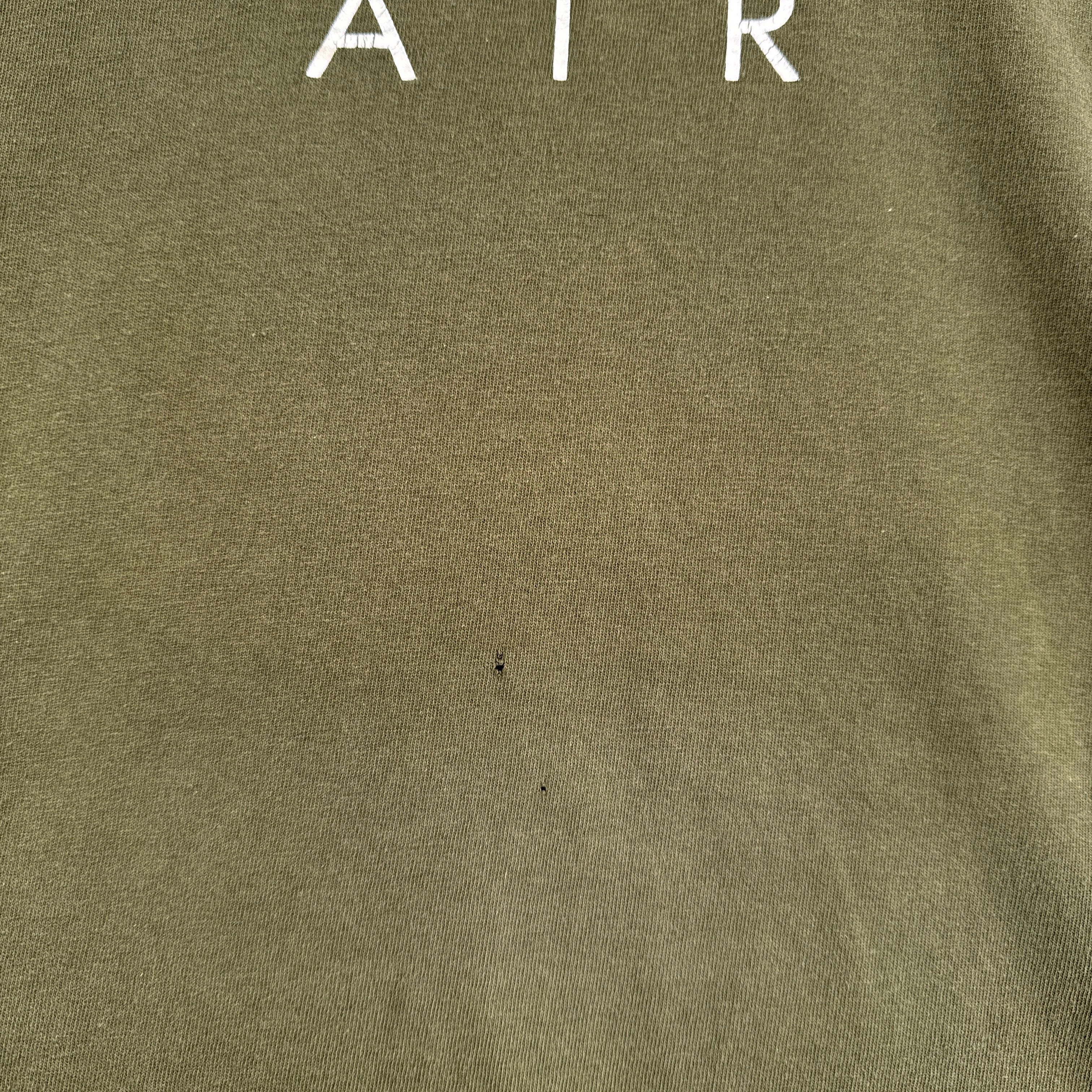 Close-up of a green fabric surface with 'AIR' text in white. 2 small holes under logo