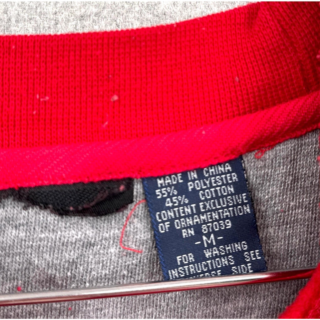 Clothing label with text on a red and gray fabric background, size Medium
