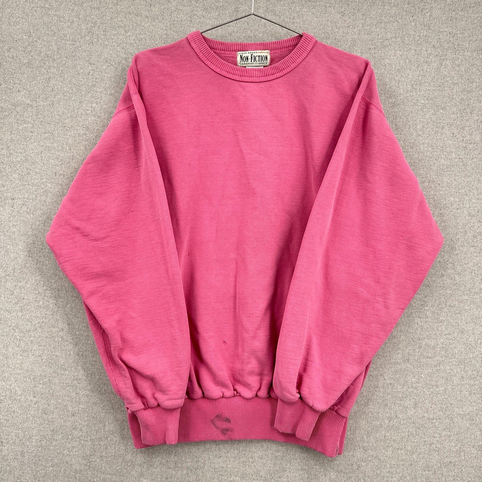 Pink sweatshirt on a hanger against a gray background