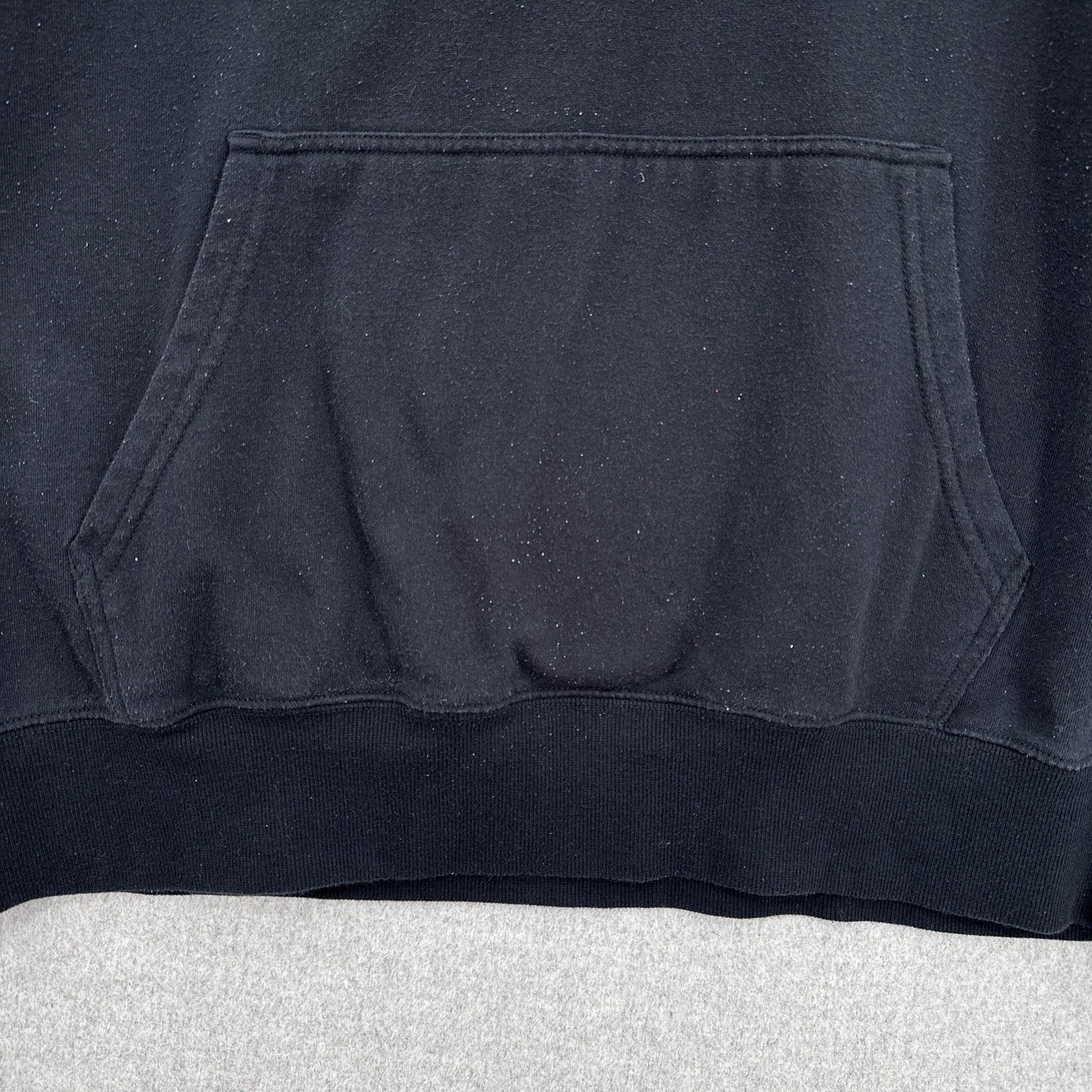 Close-up of a black hoodie with a pocket on a light gray surface
