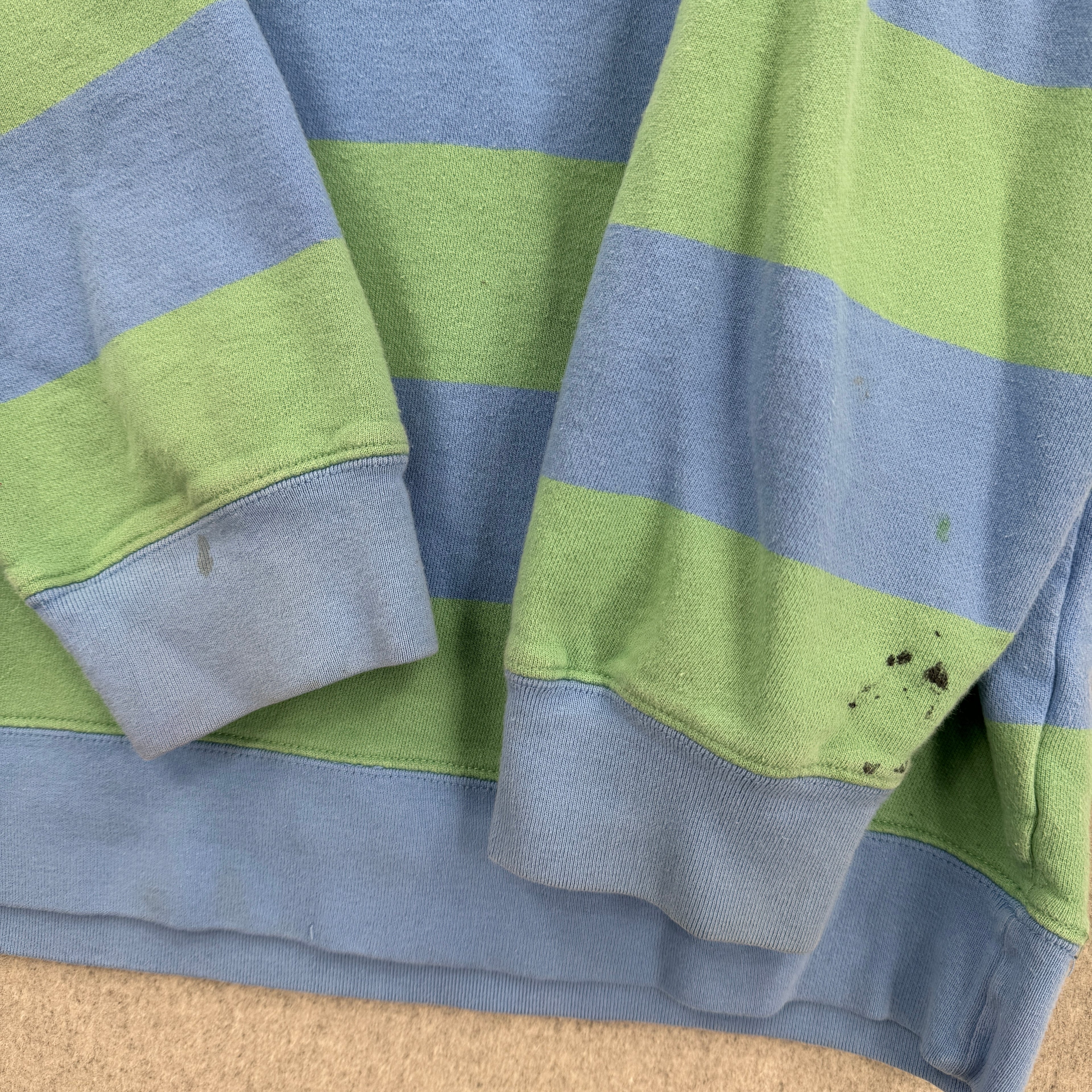 Close-up of a blue and green striped fabric with visible stains on a beige surface