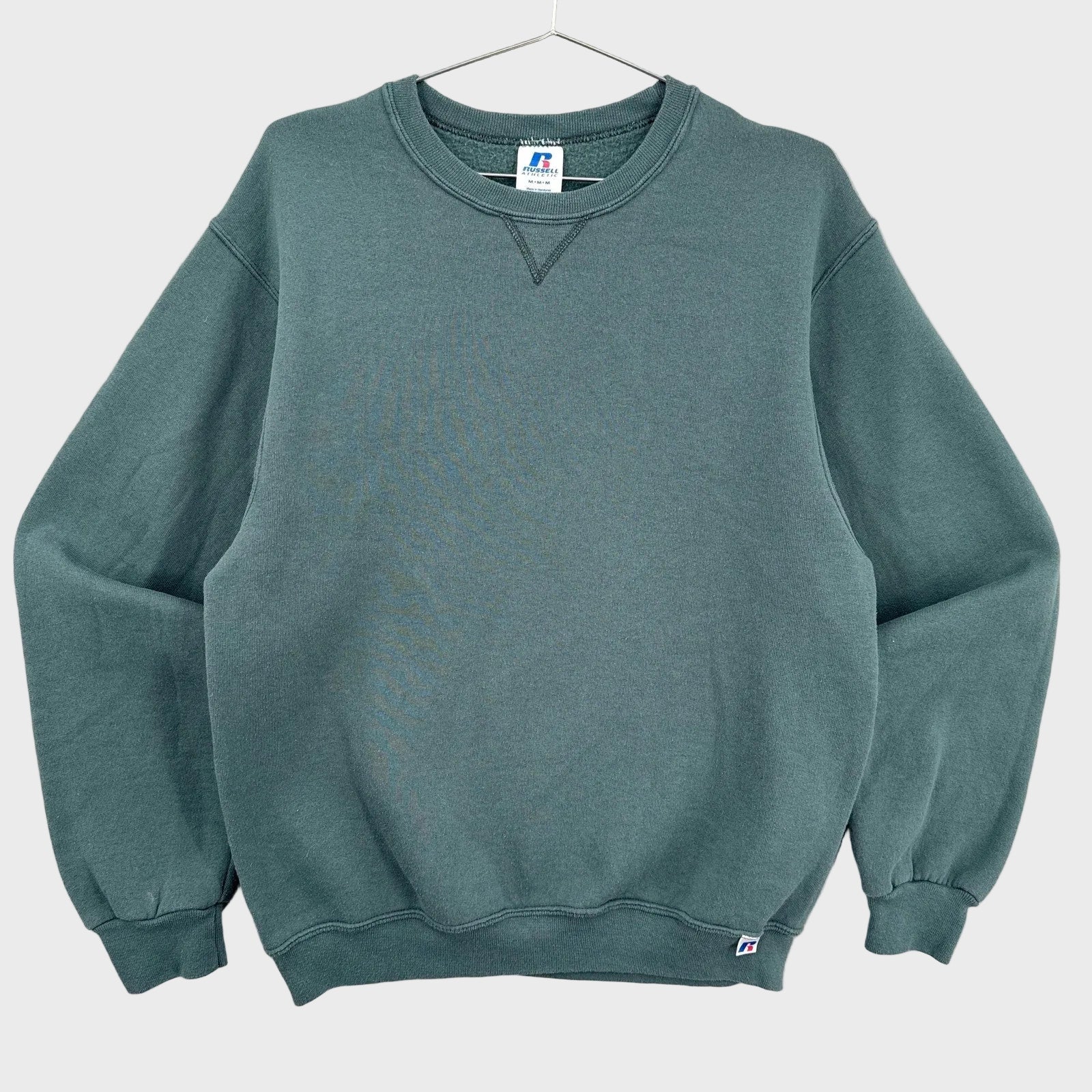Green sweatshirt on a hanger with a visible brand label against a neutral background