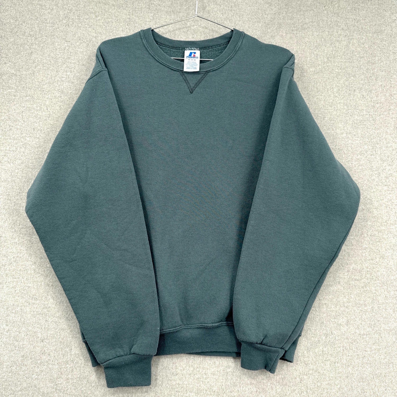 Green sweatshirt on a hanger with a visible brand label against a neutral background
