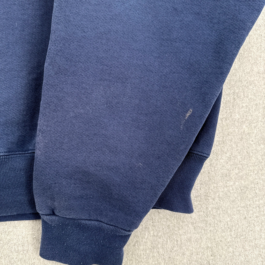 Close-up of a navy blue sweatshirt on a light gray surface. sleeve with small stain spot