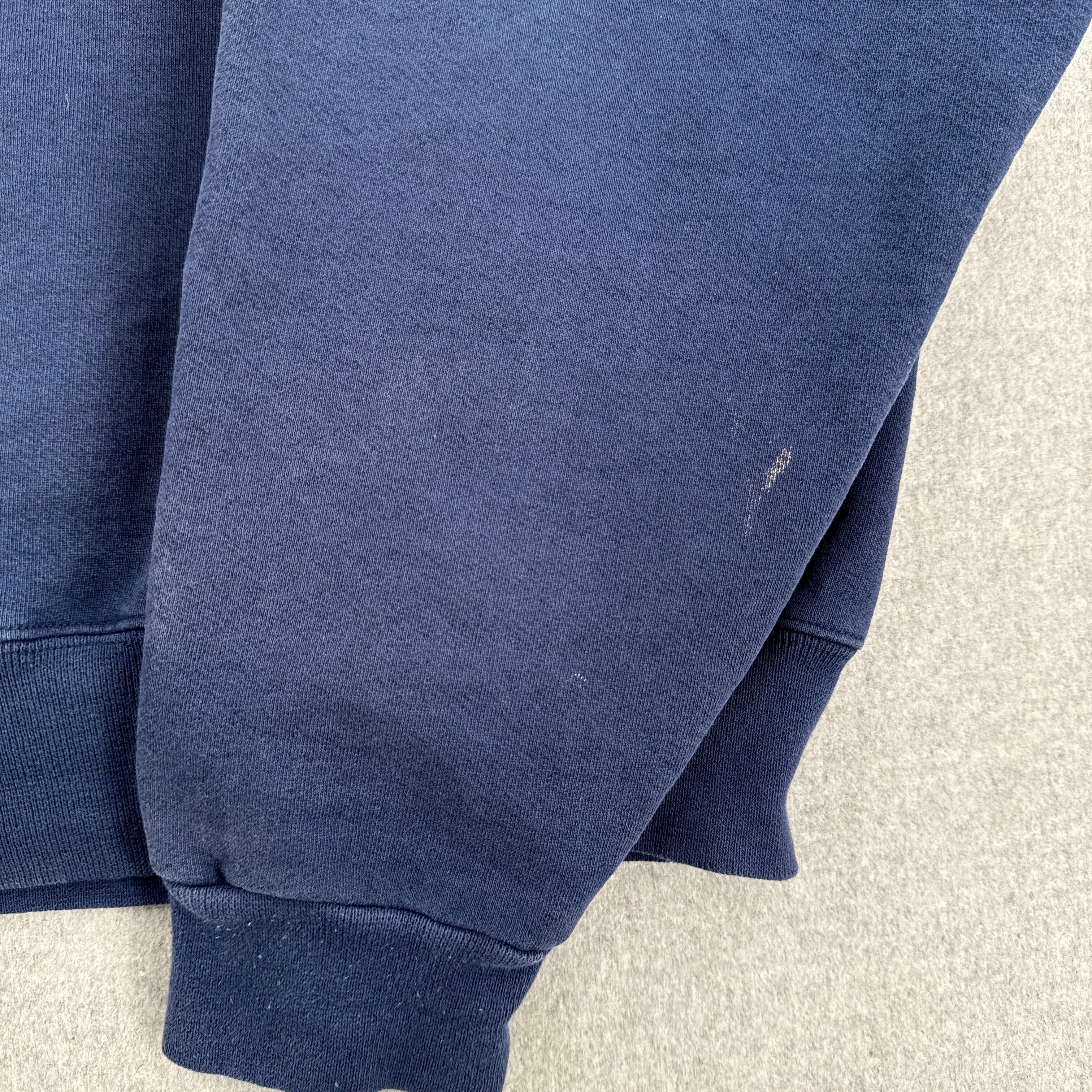 Close-up of a navy blue sweatshirt on a light gray surface. sleeve with small stain spot