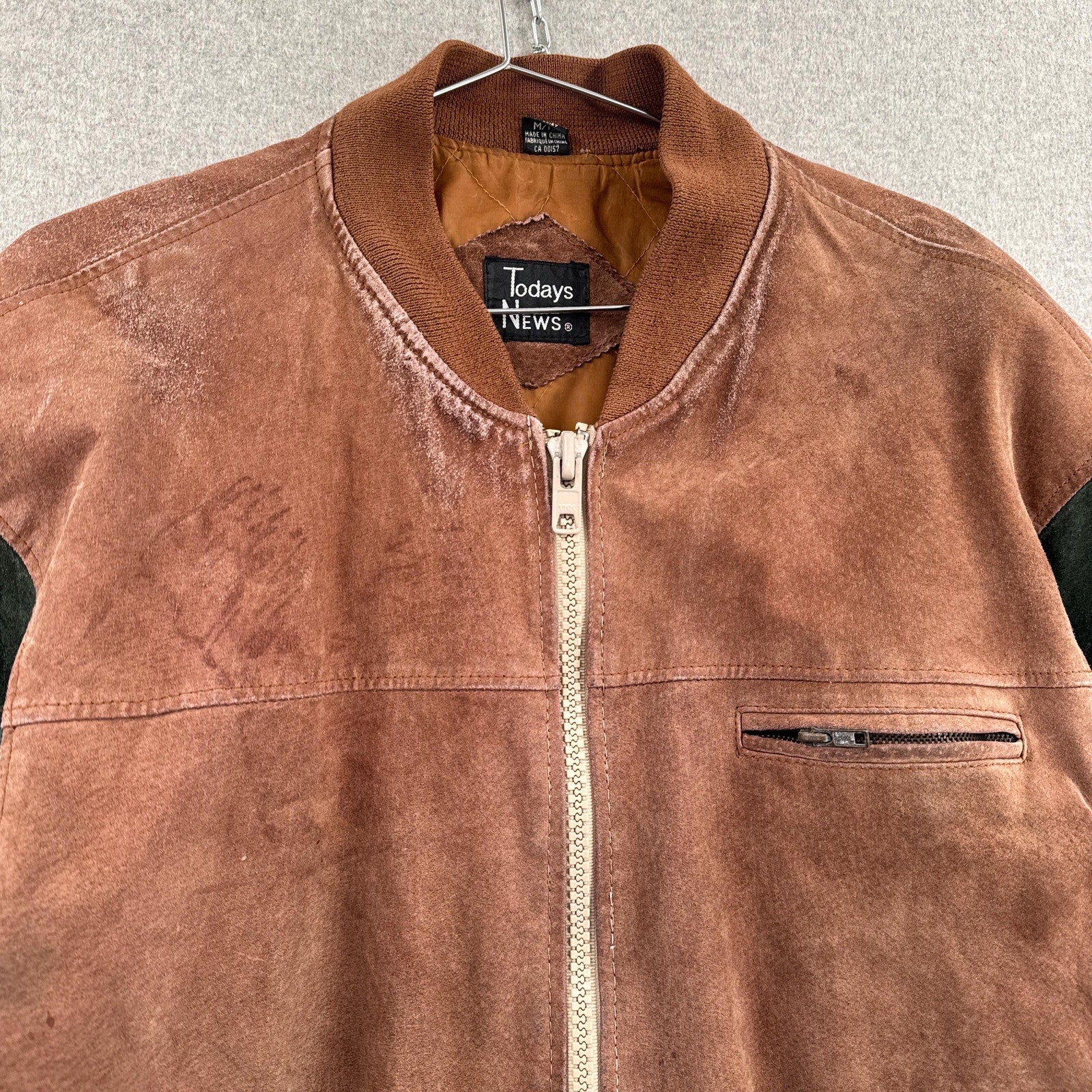 Brown jacket with a visible brand label on a hanger against a neutral background