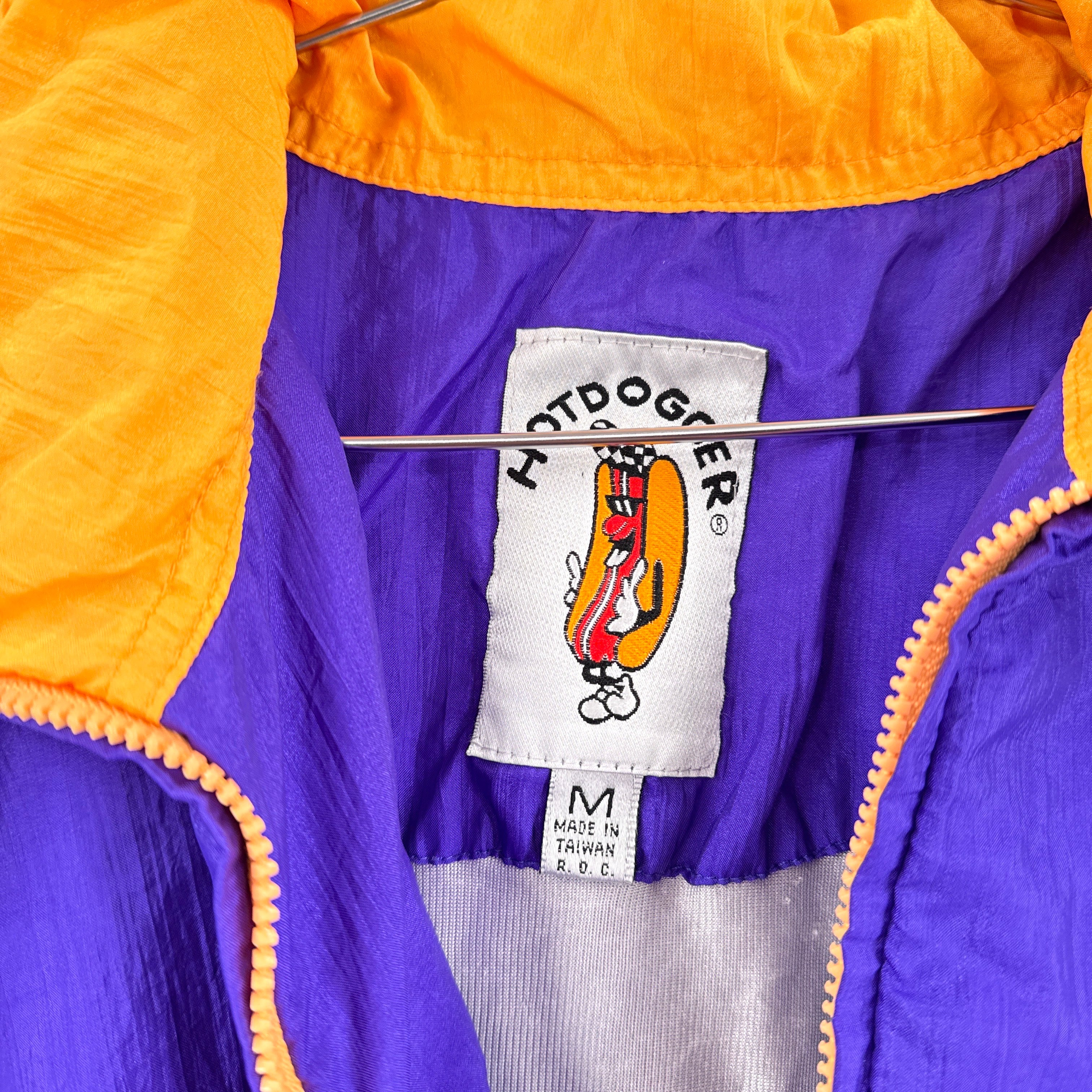 Close-up of a purple and orange jacket with a brand label featuring a hot dog graphic. tag size Medium