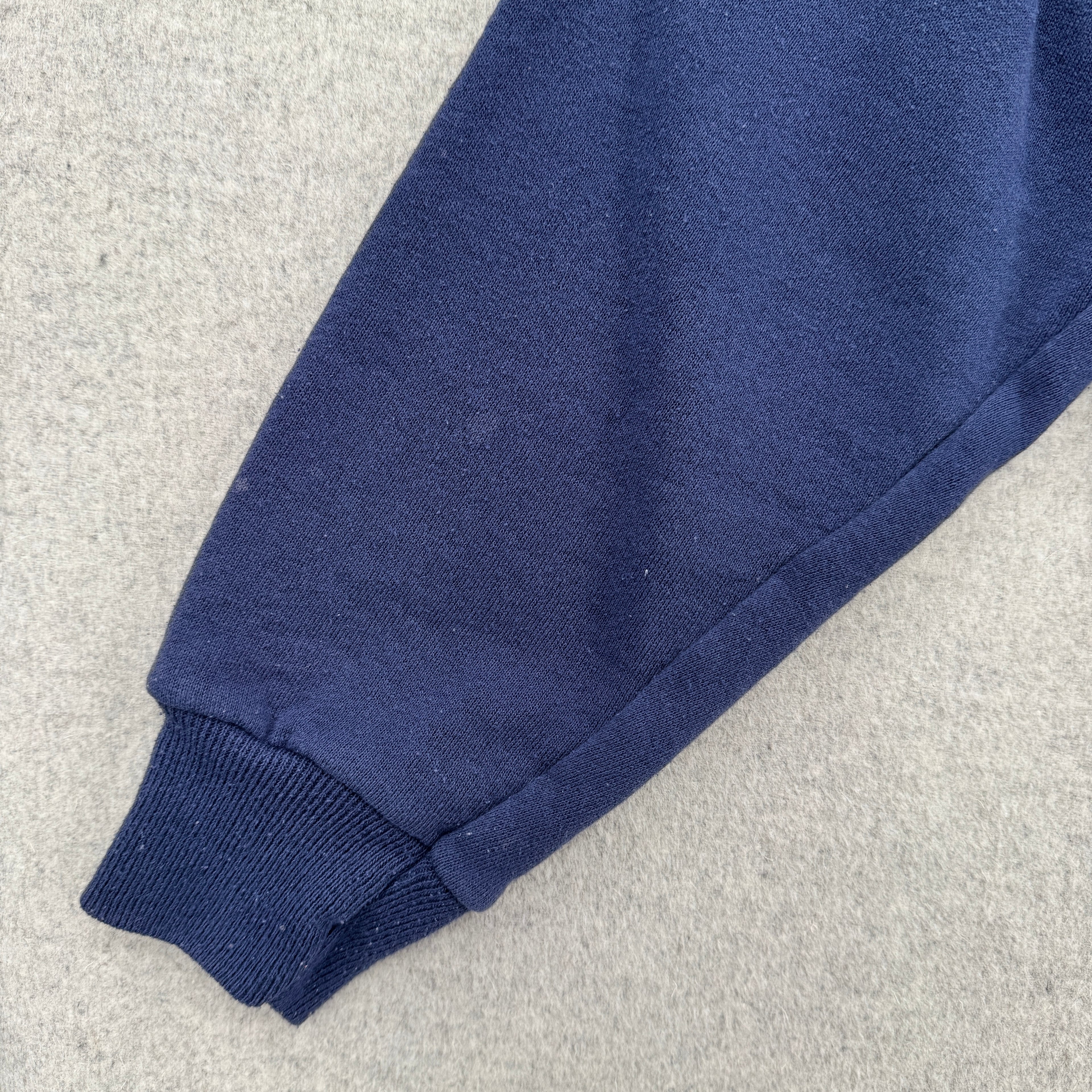 Close-up of a blue fabric sleeve on a light gray background. Shows 2-3 small lightened blue stain spots.