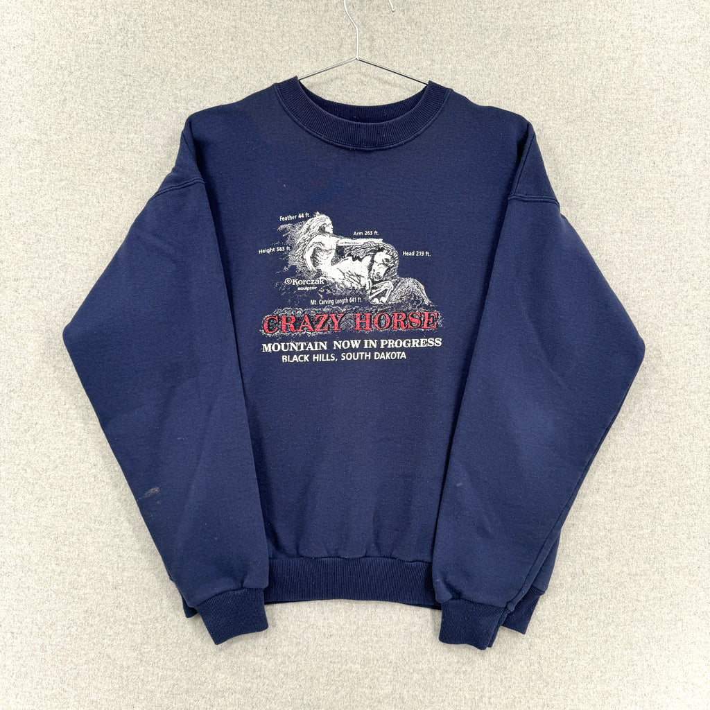 Navy blue sweatshirt with graphic design on a beige textured background. Sleeves folded over