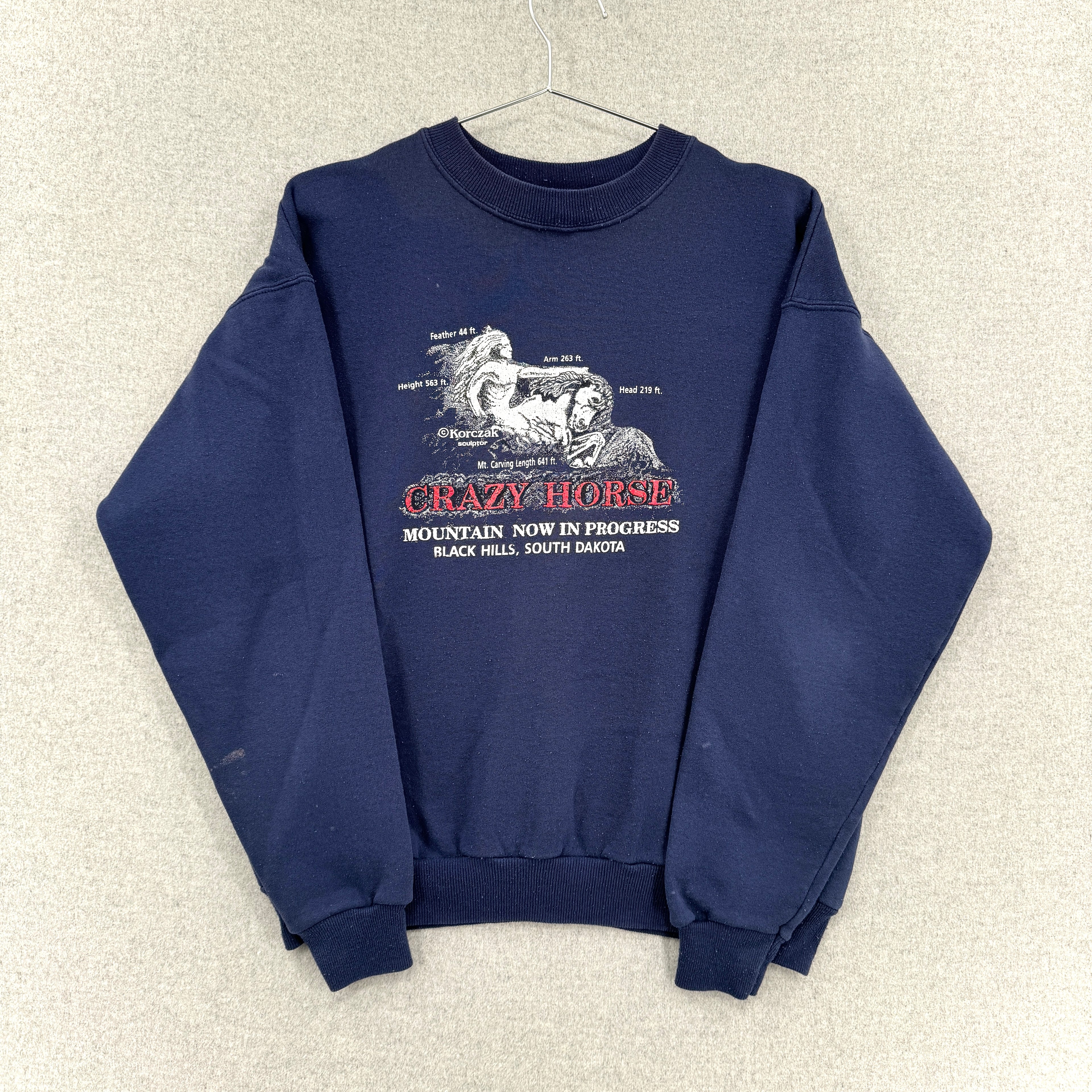 Navy blue sweatshirt with graphic design on a beige textured background. Sleeves folded over
