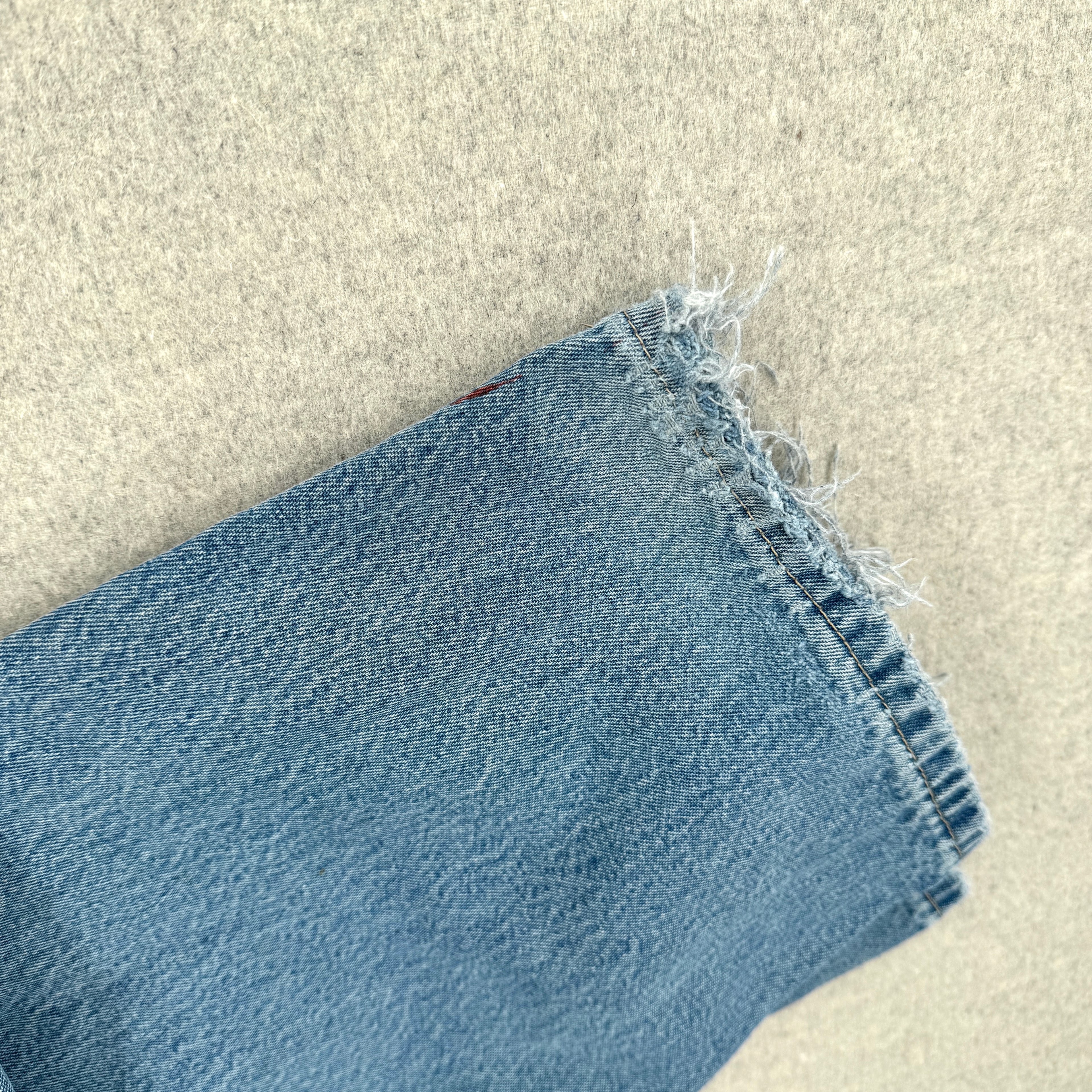 Close-up of blue denim fabric on a beige surface. frayed bottom hem 