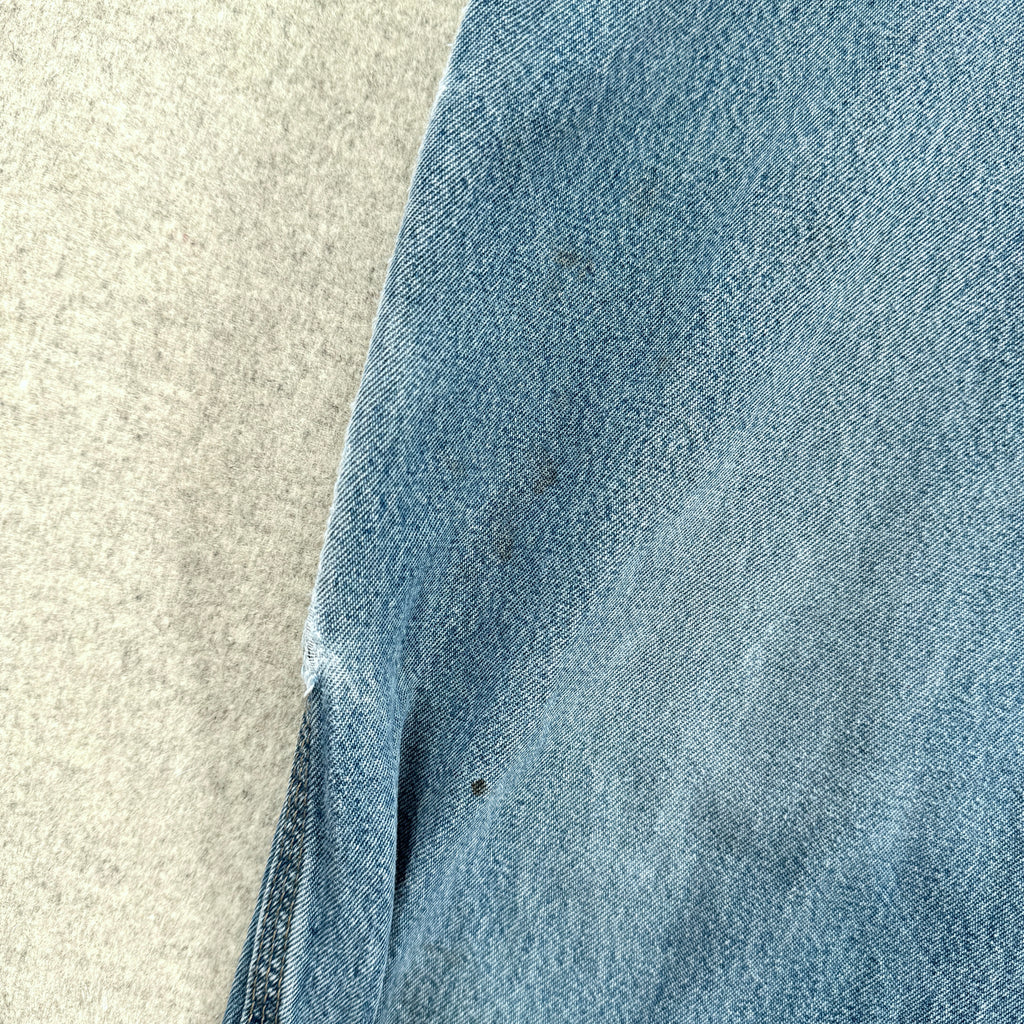 Close-up of blue denim fabric on a textured beige surface, small stain spots