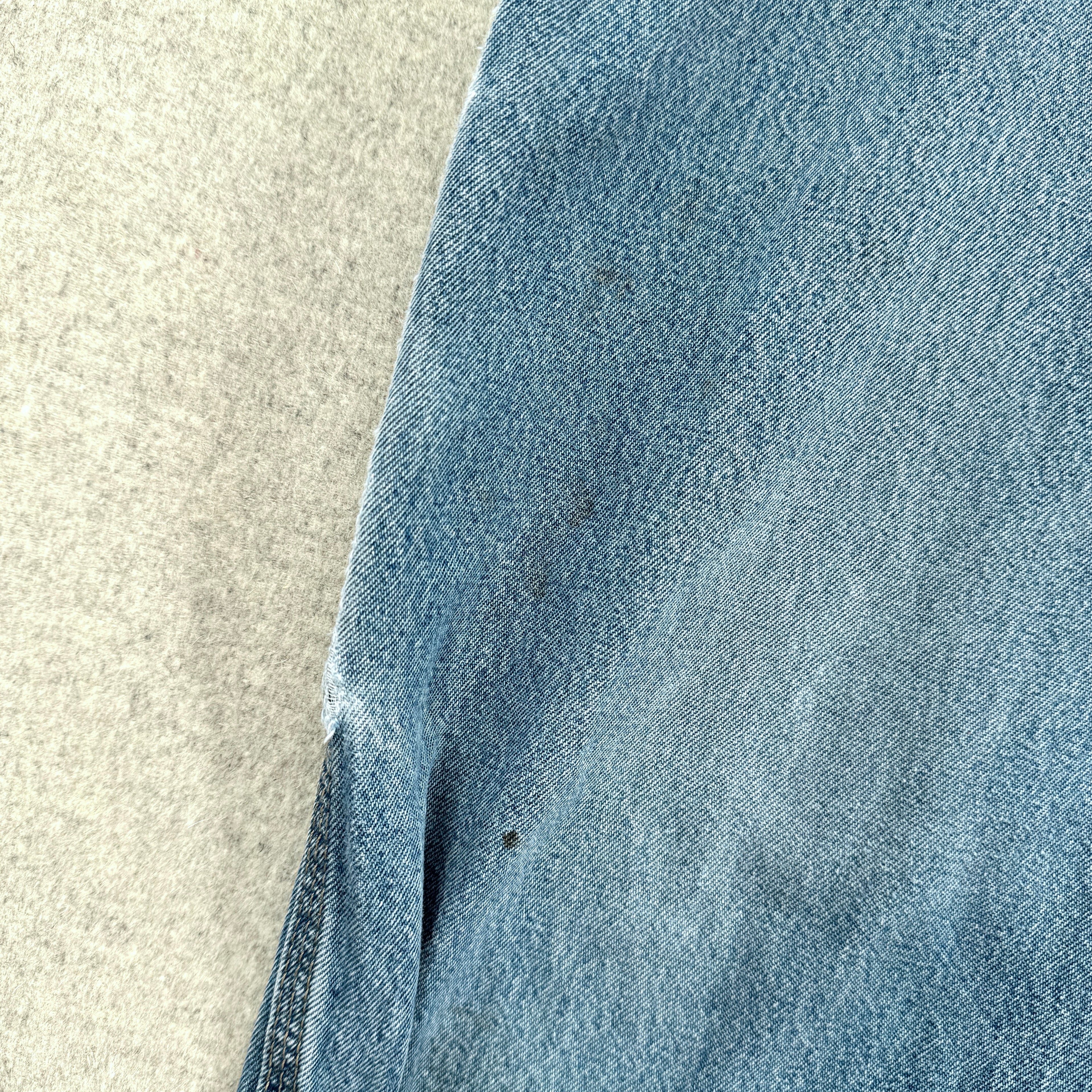 Close-up of blue denim fabric on a textured beige surface, small stain spots