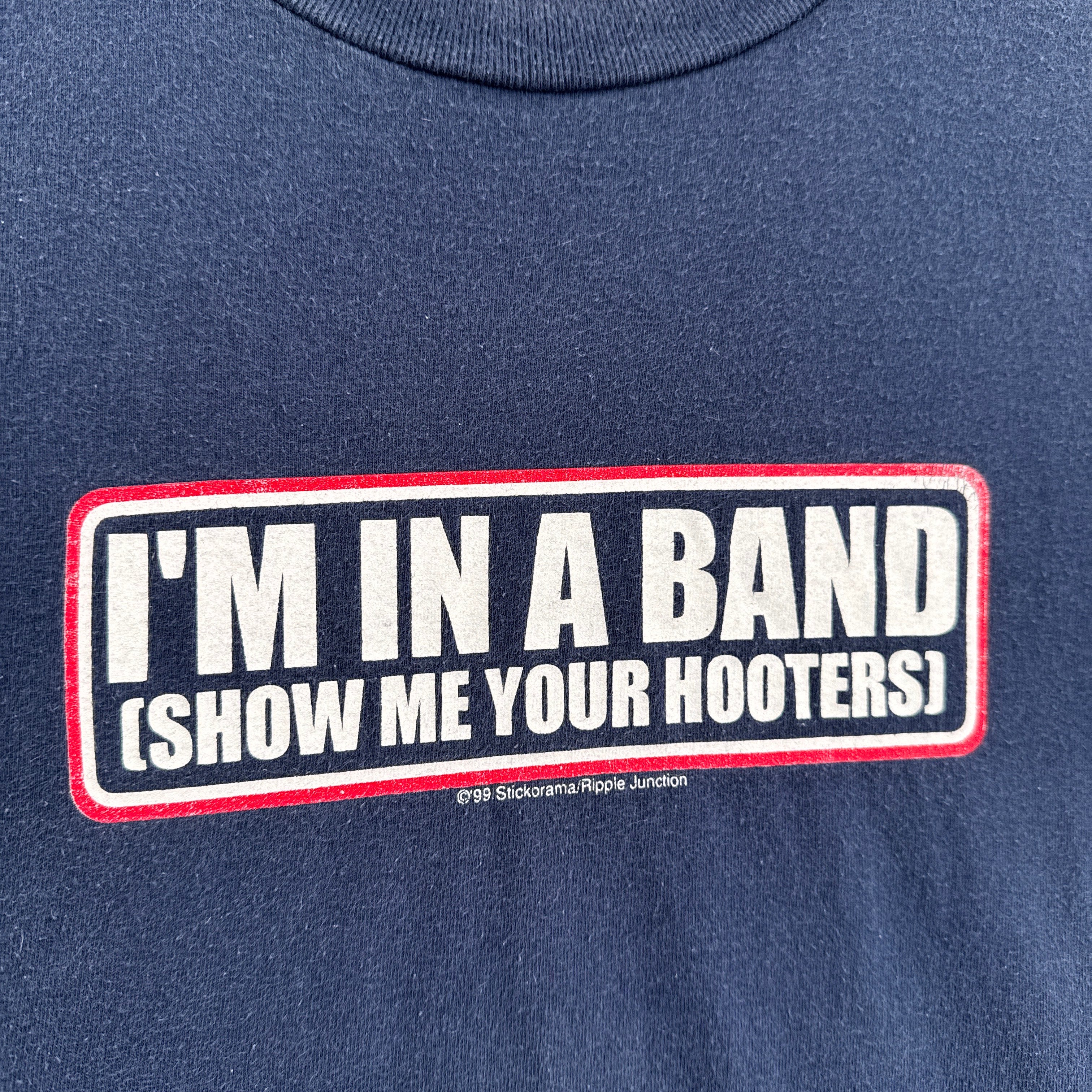 Navy blue shirt with a humorous text patch on a plain background. "I'm in a band show me your hooters"