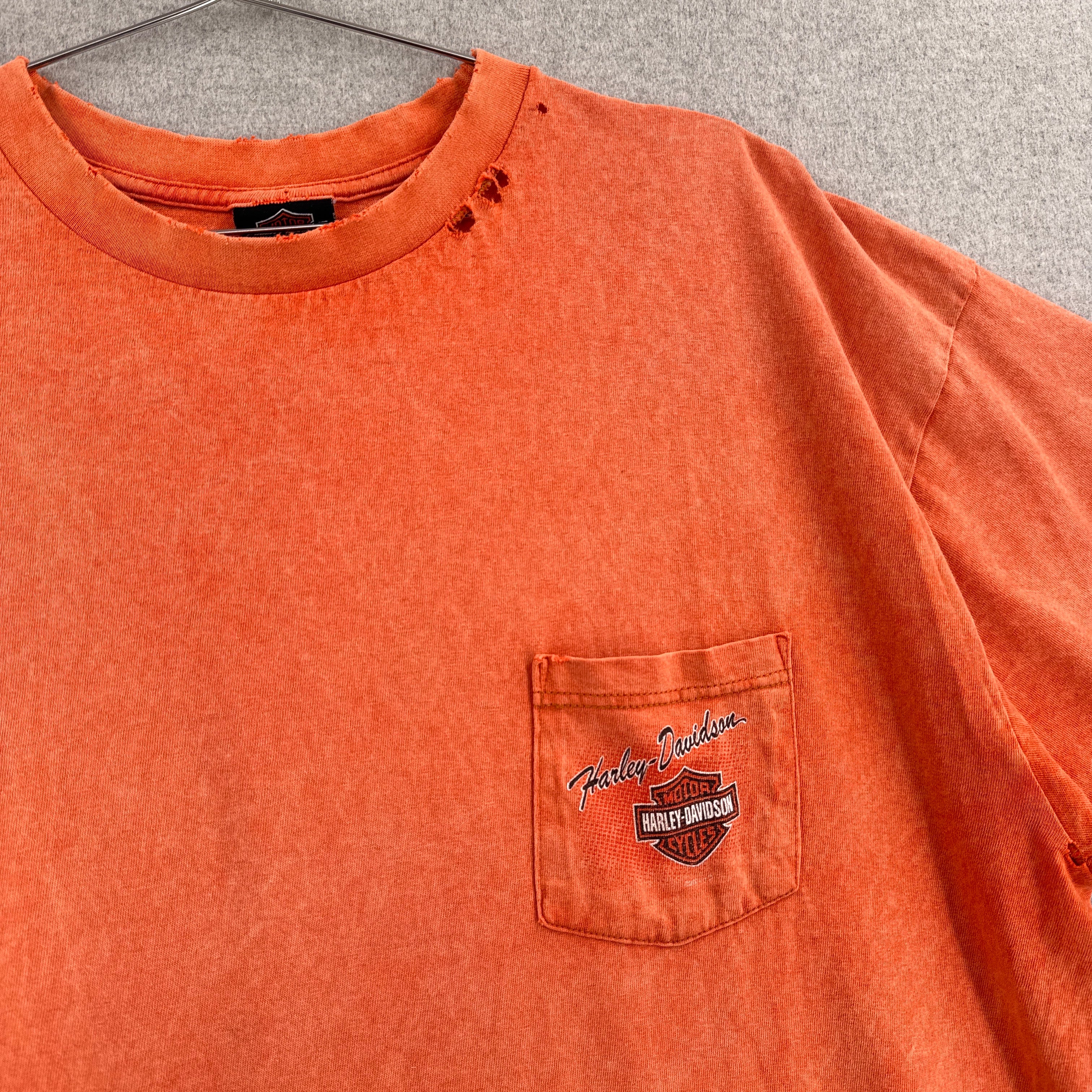 Orange t-shirt with Harley Davidson logo on a hanger against a gray background