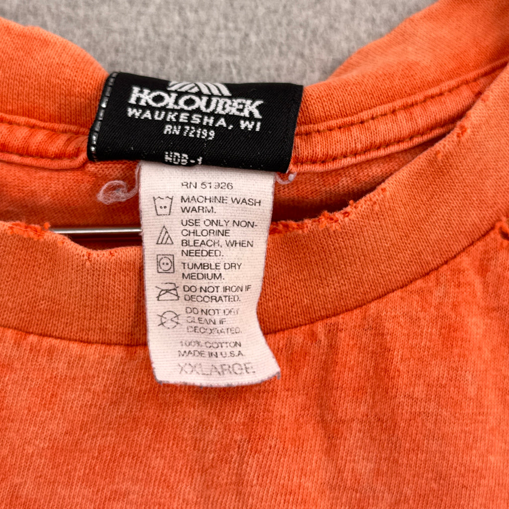 Close-up of an orange garment with a label on a gray background. tag is 2XL size, made in usa, 100% cotton