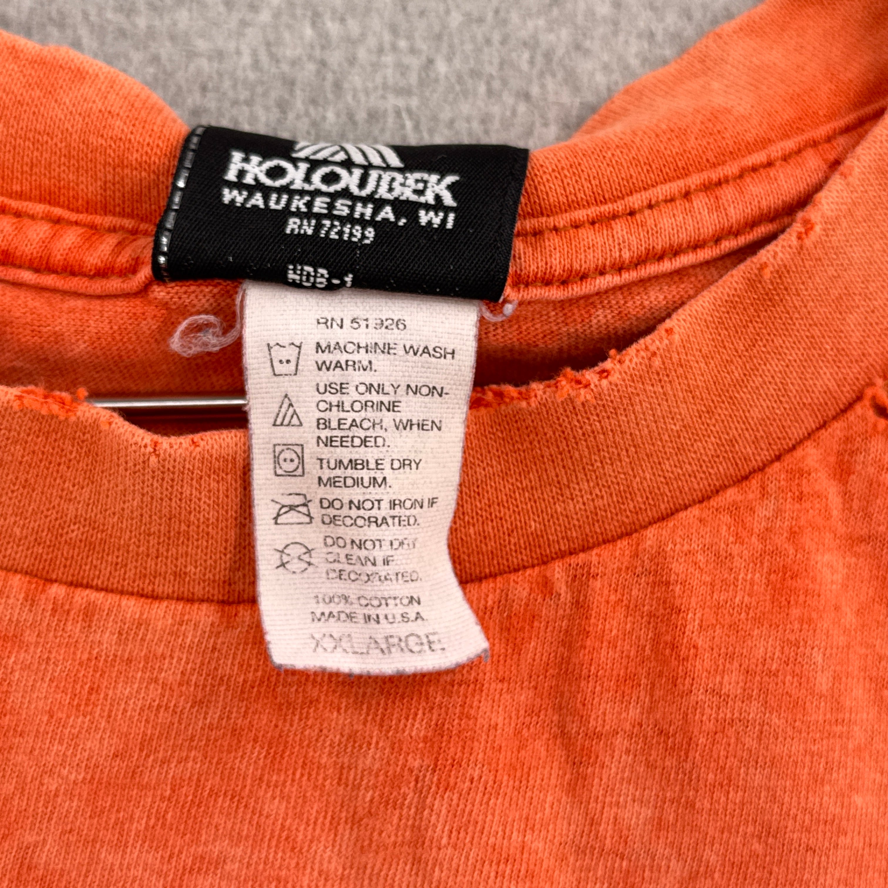 Close-up of an orange garment with a label on a gray background. tag is 2XL size, made in usa, 100% cotton