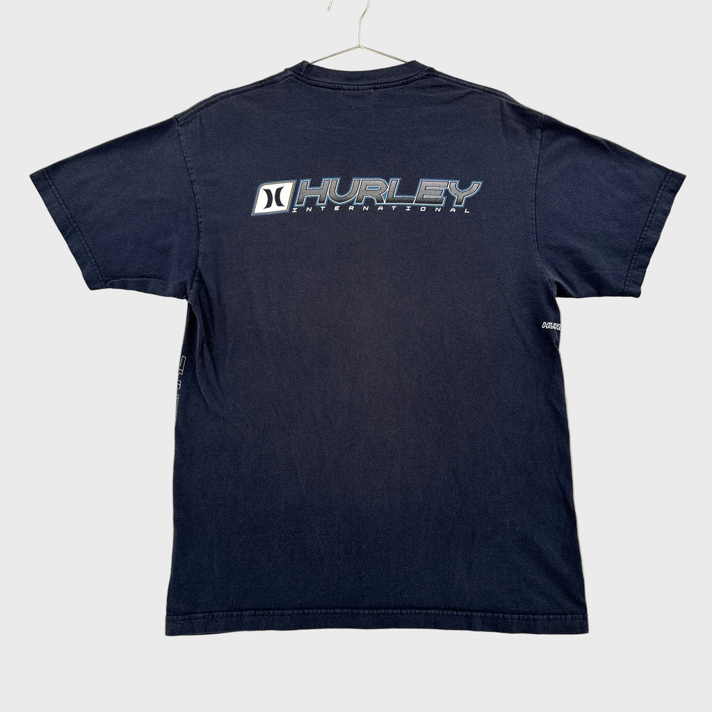 A dark navy blue short-sleeve t-shirt laid flat on a light gray textured surface. The back of the shirt features a vertical graphic print of the Hurley brand name in white and gray.