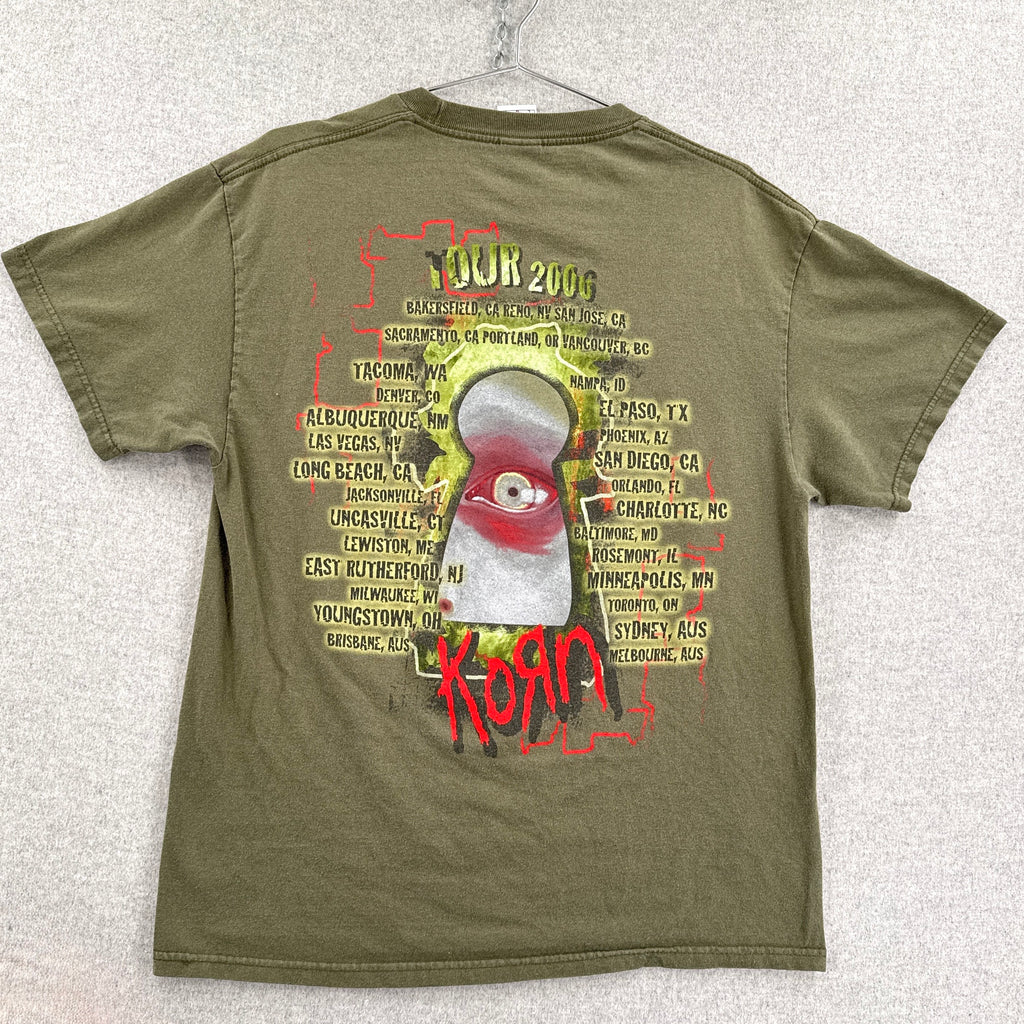 Green t-shirt with graphic design and text on a textured white background. Korn Tour 2006 US, Canada, Australia locations