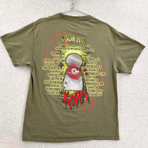 Green t-shirt with graphic design and text on a textured white background. Korn Tour 2006 US, Canada, Australia locations