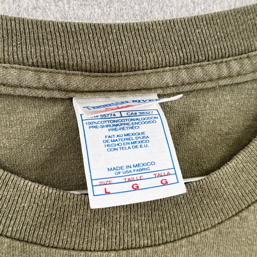 Close-up of a label on a green garment with text and a brand logo. Tennessee River tag size Large 100% cotton