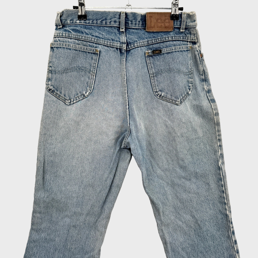 Light blue jeans hanging on a beige wall. back top showing Lee logo above pocket