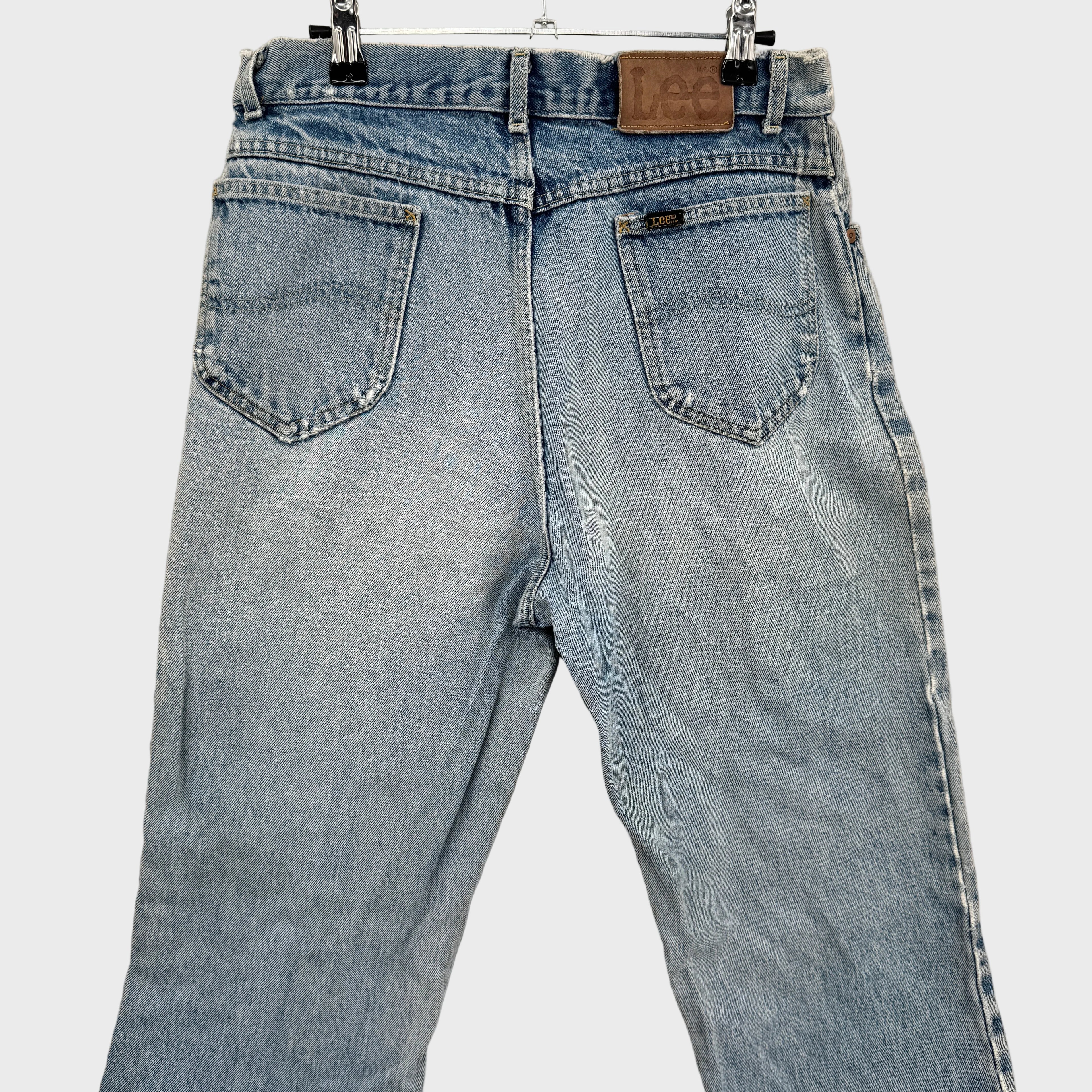 Light blue jeans hanging on a beige wall. back top showing Lee logo above pocket