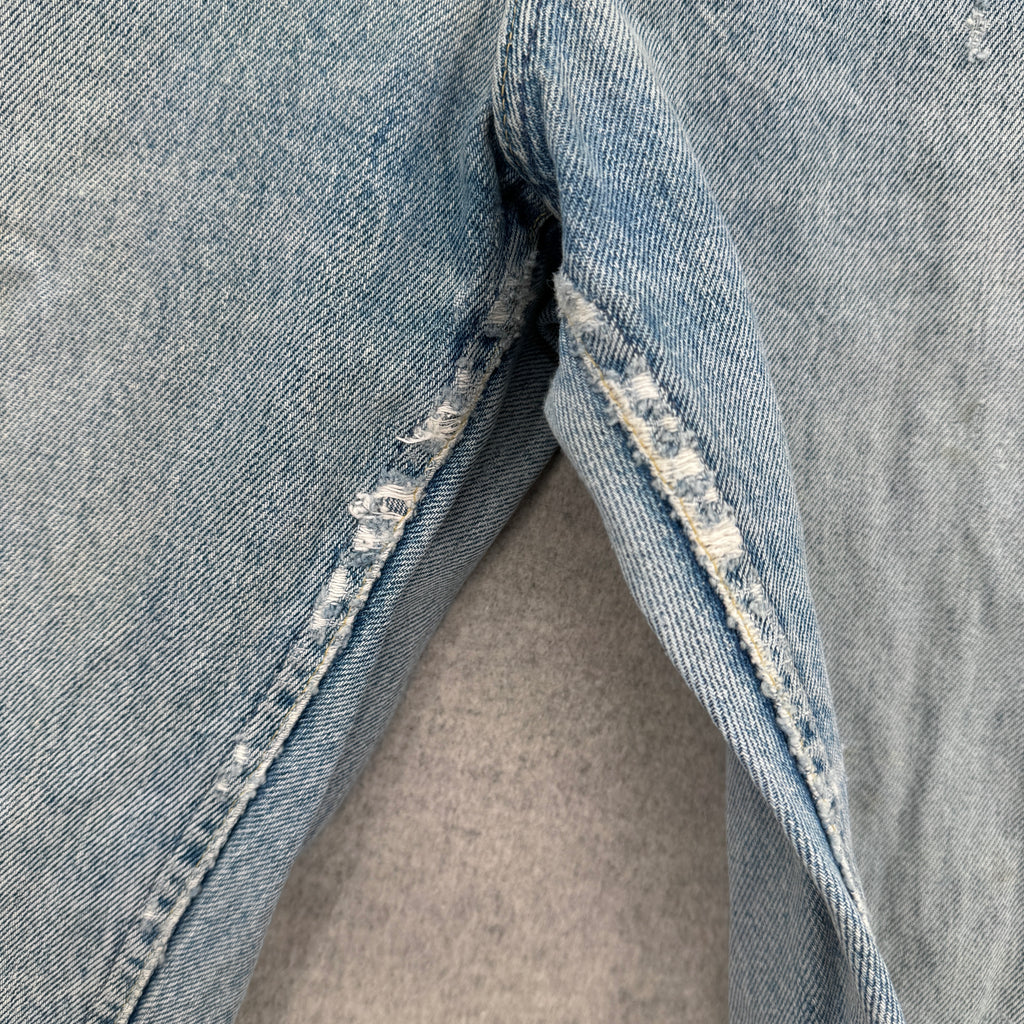 Close-up of a blue denim fabric with a pocket detail on a gray background. fraying around the crotch
