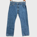 Pair of blue jeans hanging on a wooden hanger against a beige wall.