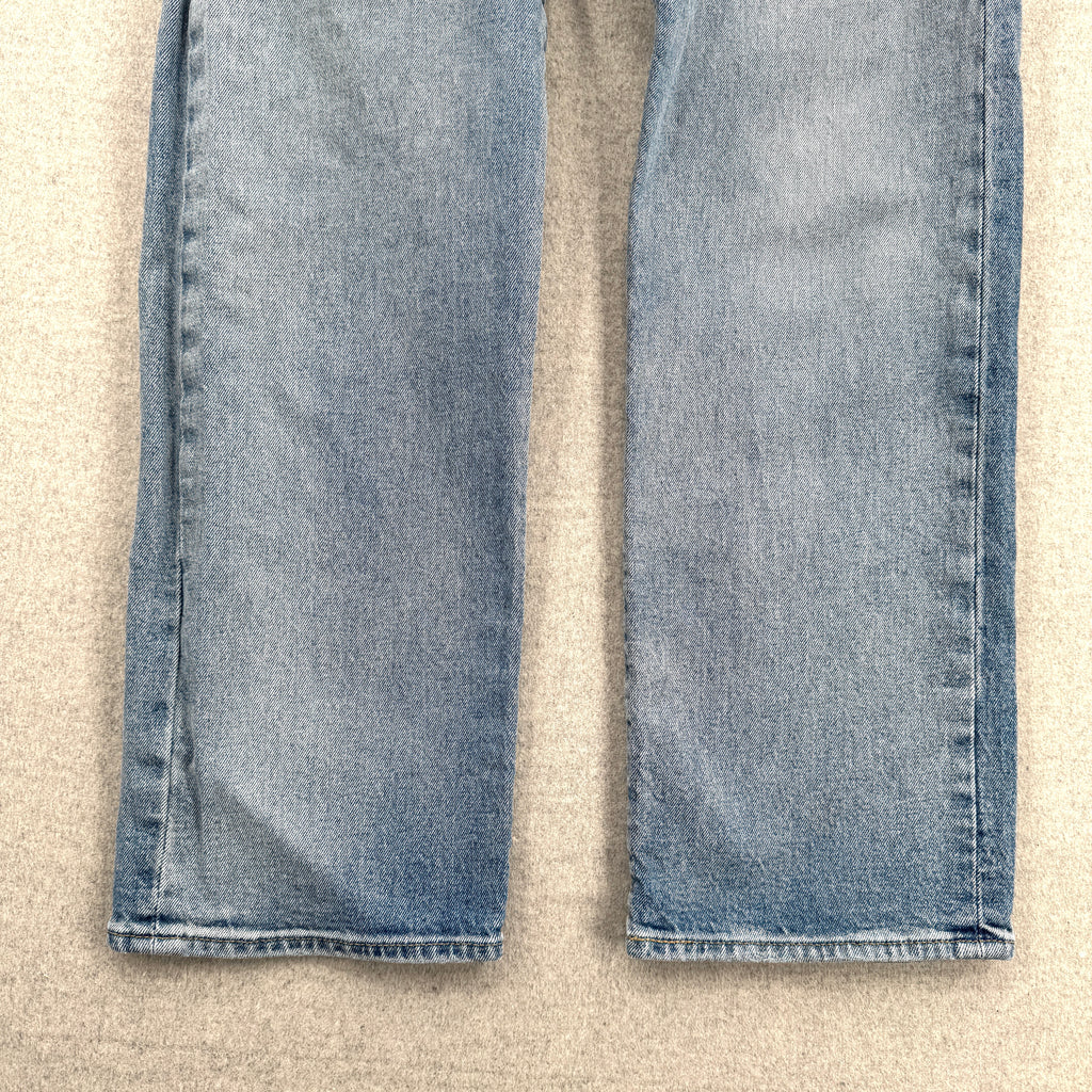 Folded blue jeans on a beige surface. Bottom of pants front