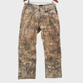 Camouflage pants hanging on a wooden hanger against a gray textured wall.