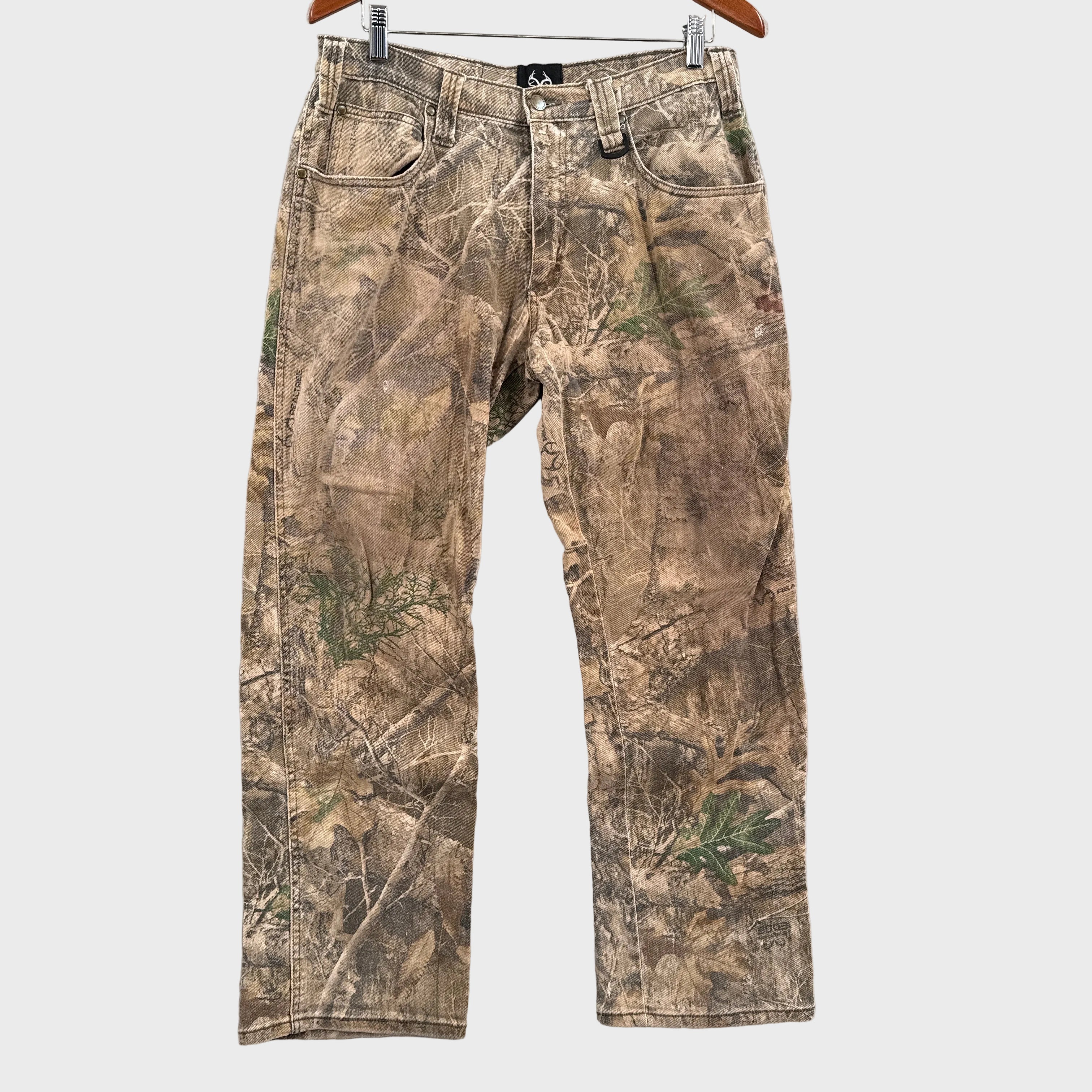 Camouflage pants hanging on a wooden hanger against a gray textured wall.
