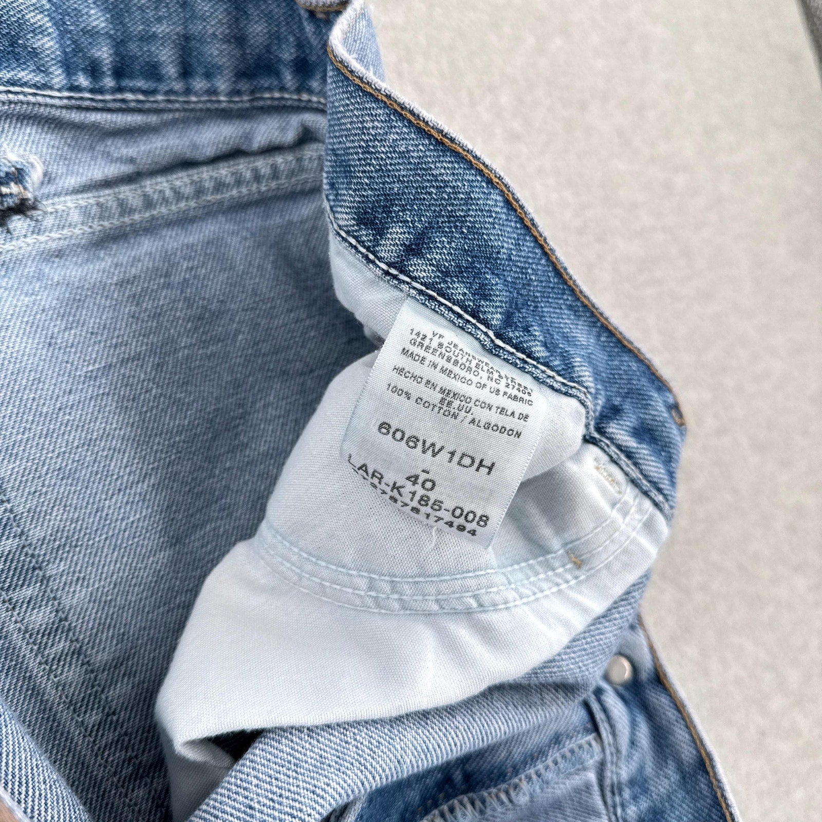 Close-up of a denim jacket with a brand label on a light gray background. Tag size 40